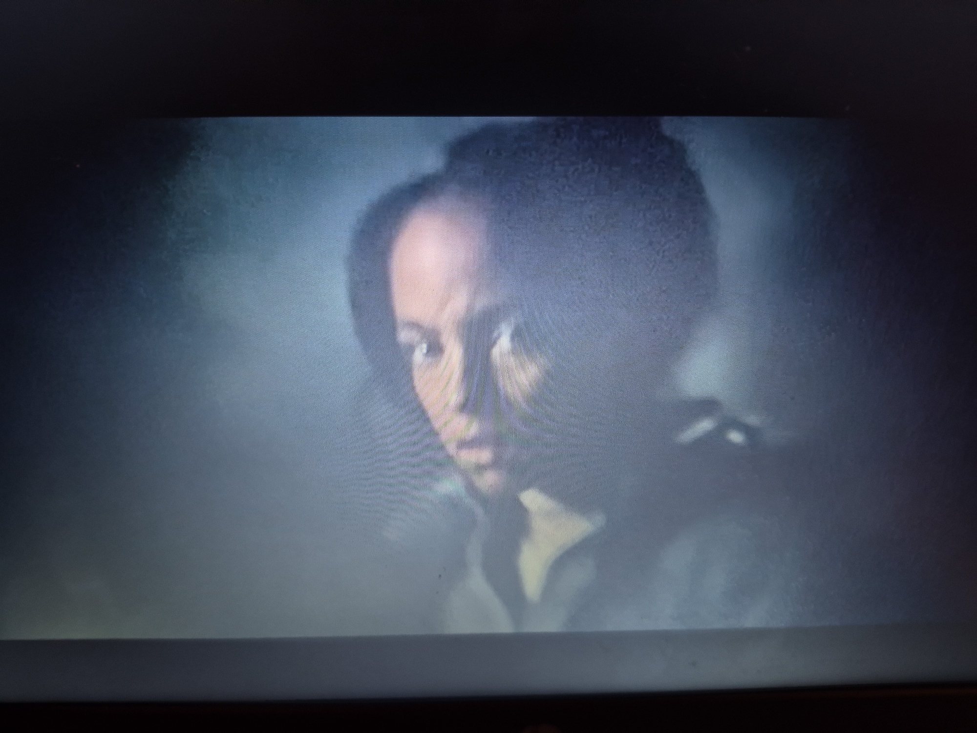 The image is a low-resolution, slightly out-of-focus photograph of a person's face, partially illuminated by light. The person appears to have dark skin and is looking towards the viewer. The background is dark and indistinct. There is no discernible location within the city of Sandwell, United Kingdom, visible in this image. The scene is static and no actions or interactions are depicted.