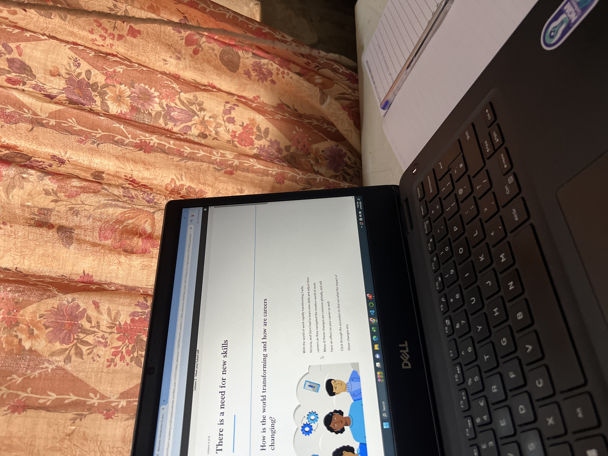 A partially-viewed laptop sits on a surface with a red and beige floral patterned cloth partially beneath. The laptop's screen displays text stating "There is a need for new skills. How is the world transforming and how are careers changing?". A black Dell keyboard is visible on the right side of the laptop. To the right of the laptop, partially visible, is a notebook with lined paper and a pen. The laptop's screen also displays the phrase "Congratulations on your convocation." There is no indication in the image that would specify the location as the city of Minna, Nigeria.
