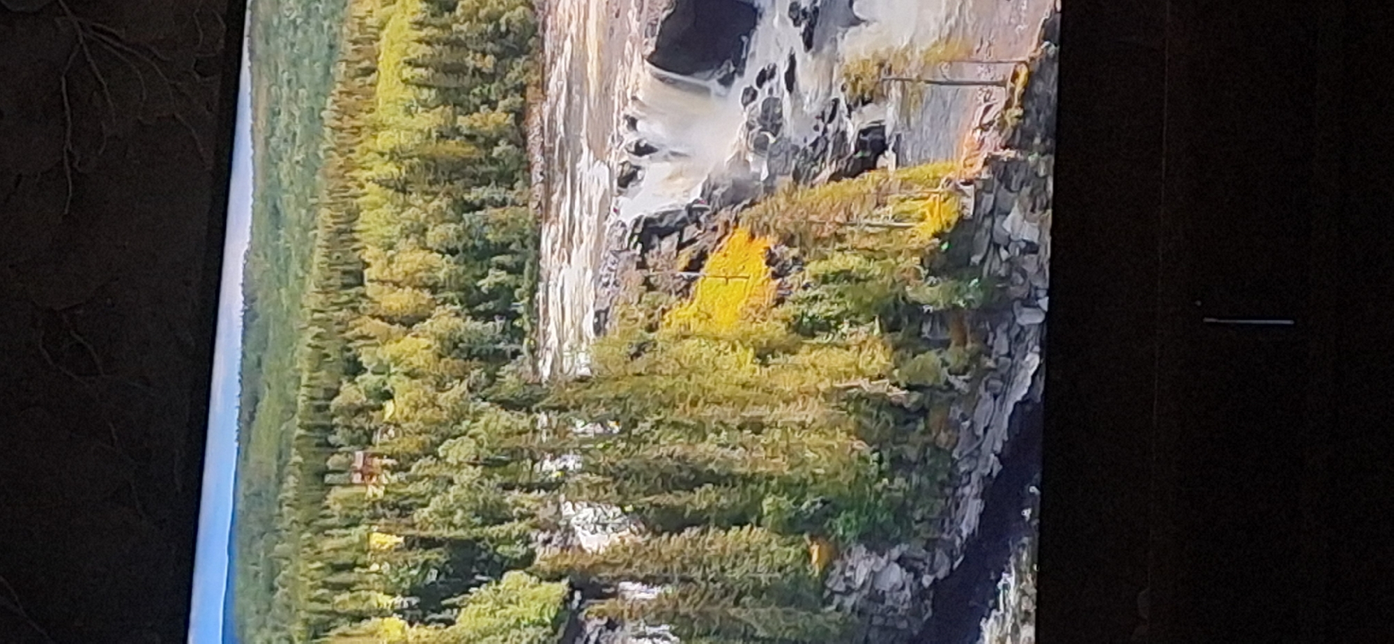 The image depicts a natural landscape featuring a wide river with cascading waterfalls. The riverbanks are lined with lush green and yellow foliage, characteristic of a forest. Rocky formations and steep cliffs are visible along the river's edge. The scene is dominated by trees, with a dense forest covering the background. The sky is clear and blue, suggesting fair weather. There is a small, reddish-brown building visible amidst the trees in the upper left portion of the image. The overall impression is one of a serene and wild natural environment.
This image does not depict the city of Bila Tserkva, Ukraine. The scene is a natural landscape, likely a river or waterfall area, with no identifiable urban elements or landmarks associated with Bila Tserkva.