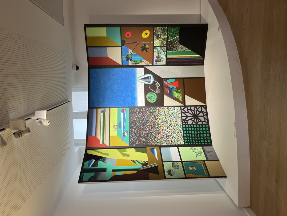 The scene depicts a contemporary art installation within a gallery space at the Centre Pompidou, Musée National d'Art Moderne, in Paris, France. Dominating the foreground is a large, multi-paneled artwork titled "Le grand tableau des arts visuels (The Great Painting of Visual Arts)" by Erró, created in 1974. The artwork is composed of numerous black-framed segments, arranged in a slightly curved screen format atop a white, curvilinear plinth. Each segment contains distinct imagery, including abstract geometric shapes, diverse patterns such as multicolored dots and green grids, stylized objects like scrolls and optical instruments, and fragmented landscapes. The color scheme is vibrant, with strong contrasts. The gallery features white walls and a light wood floor. A suspended acoustical tile ceiling is equipped with a black track lighting system holding white spotlights directed at the artwork. A white dome-shaped security camera is mounted on the ceiling in the background, where two rectangular windows are also partially visible. No individuals are present.