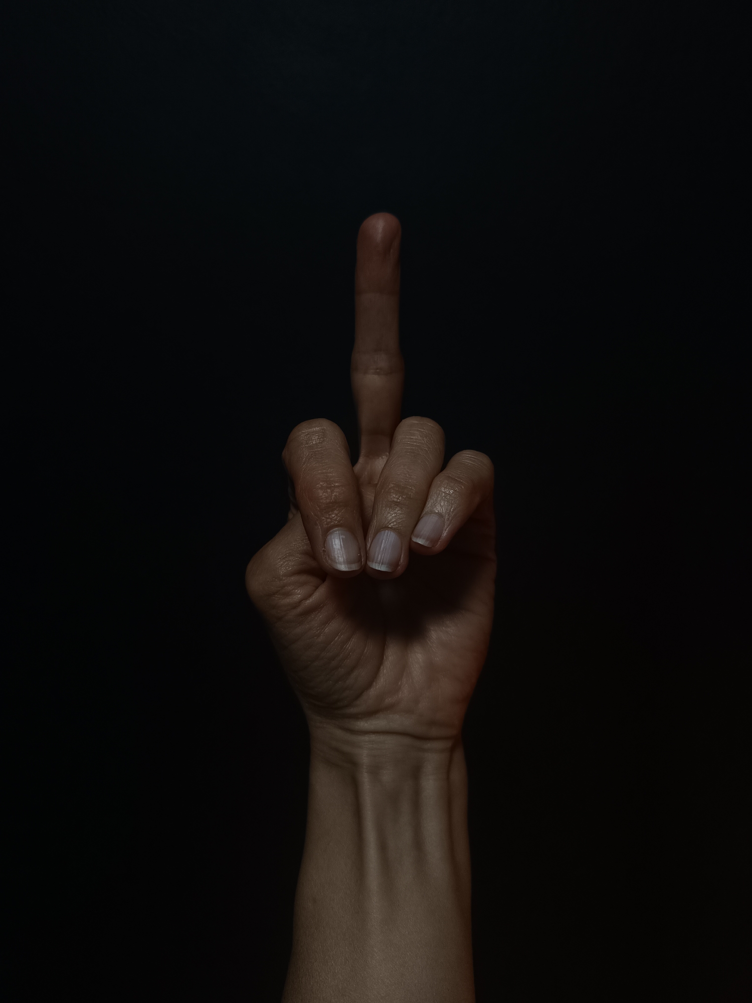 A hand is shown against a dark, seemingly featureless background. The hand is making the middle finger gesture, commonly considered an offensive or rude sign. The hand and arm are pale and appear to be those of an adult. No other identifying information is present. There is no indication that the image was taken in Lermontov, Russia or any other location.