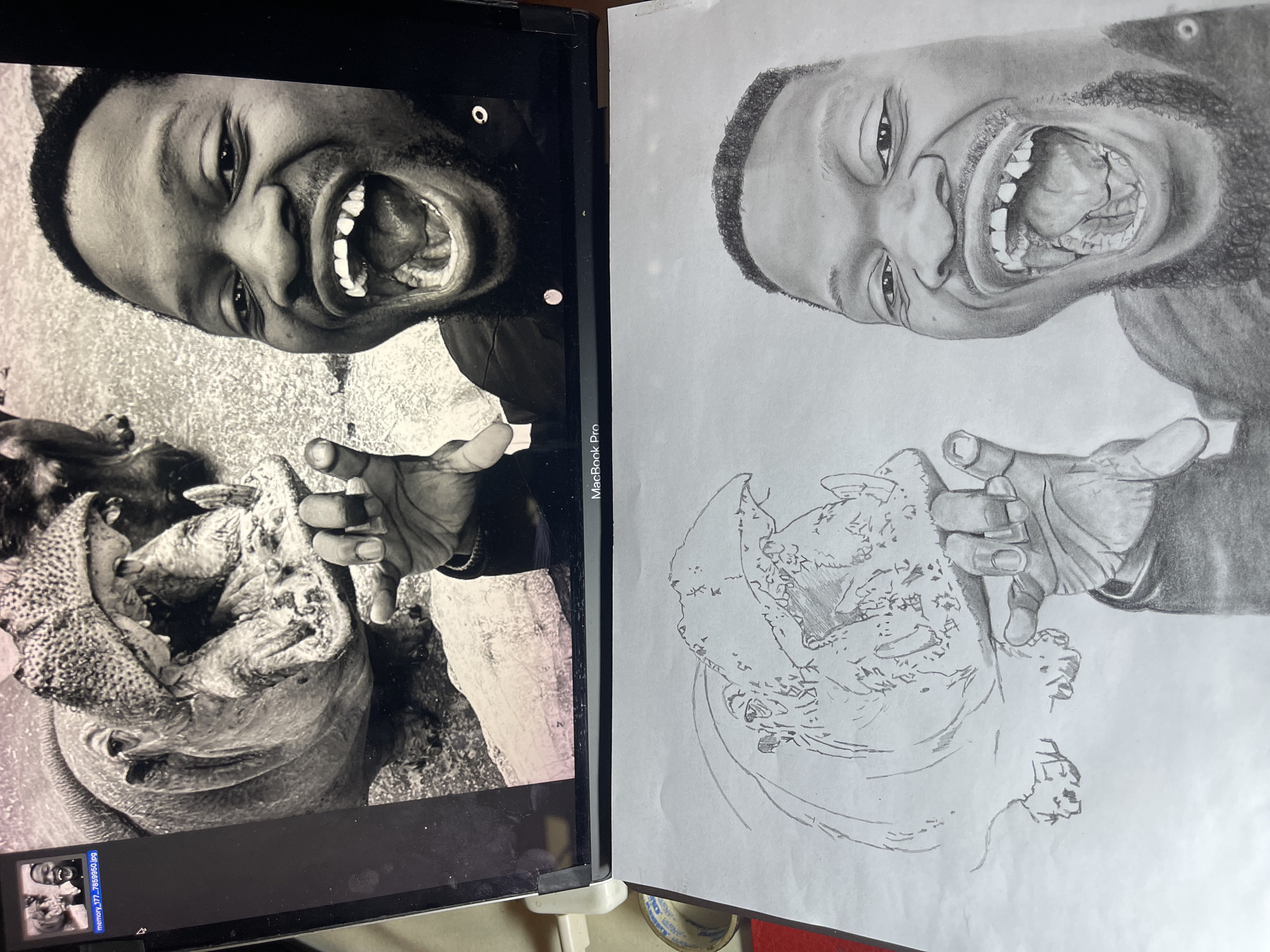 This image, captured in an indoor setting in Jos, Nigeria, displays a MacBook Pro laptop positioned above a white sheet of paper with a pencil drawing. The laptop screen shows a black and white photograph depicting a man, visible from the chest up on the right, laughing with his mouth wide open, exposing missing upper front teeth. His left hand is partially visible, fingers curled. To the left and behind the man is a large hippopotamus with its mouth agape, showcasing its teeth. A smaller portion of another hippopotamus is visible in the upper left. A file thumbnail, 'memory_177...7859950.jpg', is also present on the screen. The paper below features a detailed pencil drawing in progress, replicating the photograph. The drawing accurately renders the man's laughing expression, missing teeth, and partially visible hand. The hippopotamus is outlined with initial shading on the left side of the drawing. Partially visible in the lower left background are a blue and white patterned bowl and a red object.