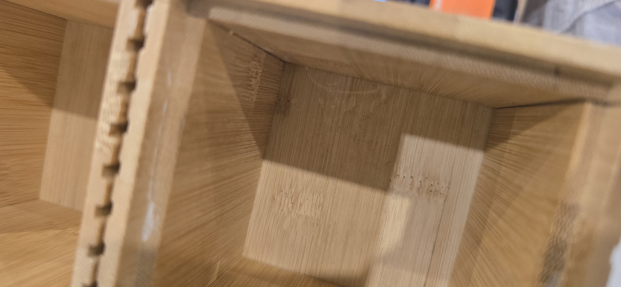 The image shows the inside of a light-colored wooden structure, possibly a shelf or drawer, with visible wood grain. A series of regularly spaced notches run along a vertical piece on the left. There's a shadow and a line of small holes on the interior surface. The location is not specified in the image, and no information is available to conclude the place.