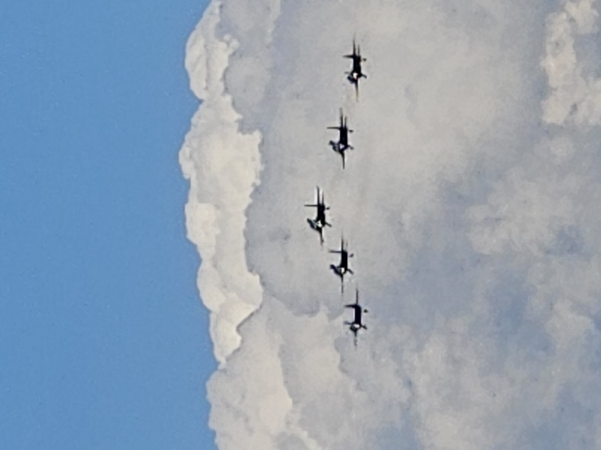 A formation of five dark-colored propeller aircraft flies against a backdrop of a bright blue sky and fluffy white clouds. The aircraft are arranged in a staggered pattern, with some appearing slightly higher or lower than others. The planes are small in the frame, suggesting they are at a significant distance. The lighting suggests it is daytime, with the sun illuminating the clouds from above. No people or specific landmarks are visible in the image. The location of Ulyanovsk, Russia is not determinable from the visual information provided.