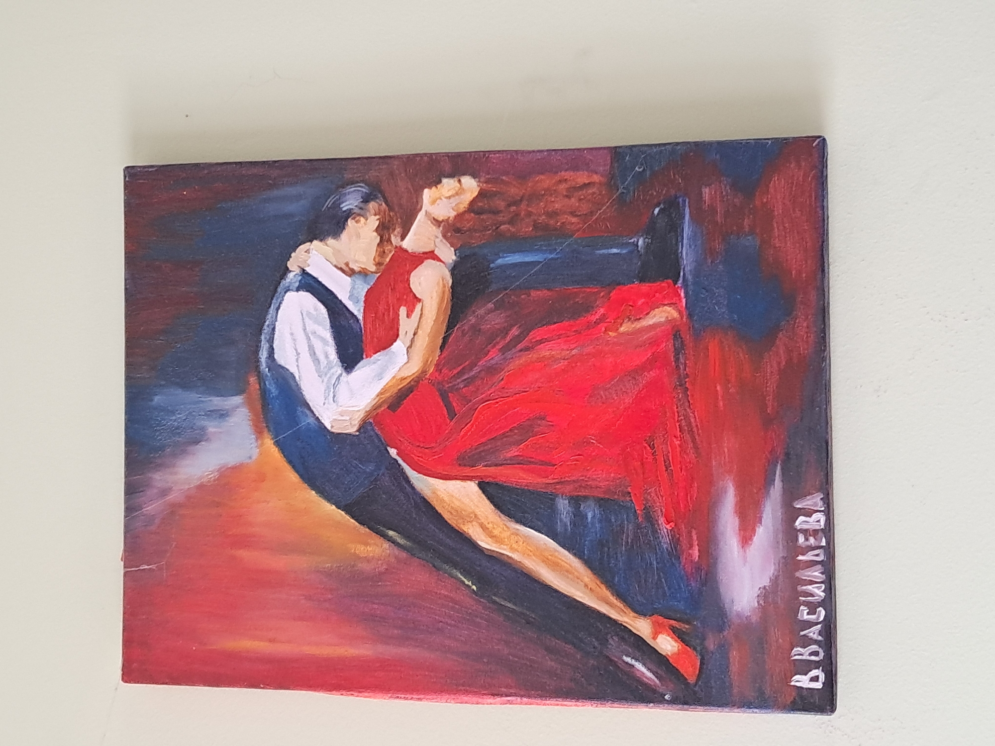 This media file features a painting depicting a couple engaged in a passionate dance, likely tango. The artwork is characterized by an expressive style with visible brushstrokes and bold colors.
**Subjects:** The main subjects are a man and a woman, shown in an intimate dance embrace. The man wears a dark waistcoat over a white shirt, while the woman is dressed in a striking red, flowing gown with a visible red high-heeled shoe on her extended foot. The background is abstract, composed of dark blues, reds, and blacks, creating a dramatic and intense atmosphere.
**Activity or event taking place:** The couple is dancing, with the man holding the woman close and her leg gracefully extended. Their posture suggests a deep connection and emotional intensity.
**Notable details:** The painting utilizes a vibrant palette dominated by the fiery red of the woman's dress and the dark, moody blues and blacks of the man's attire and the background. The dramatic lighting and abstract background elements contribute to a sense of movement and passion, suggesting an evening or night setting indoors. The painting itself shows some minor surface scratches, particularly visible across the upper right and lower left areas.
**Visible text:** The artist's signature, "B. BACUHAЕВА," written in Cyrillic, is visible vertically along the right edge of the canvas. This translates to "B. Vasilieva."
