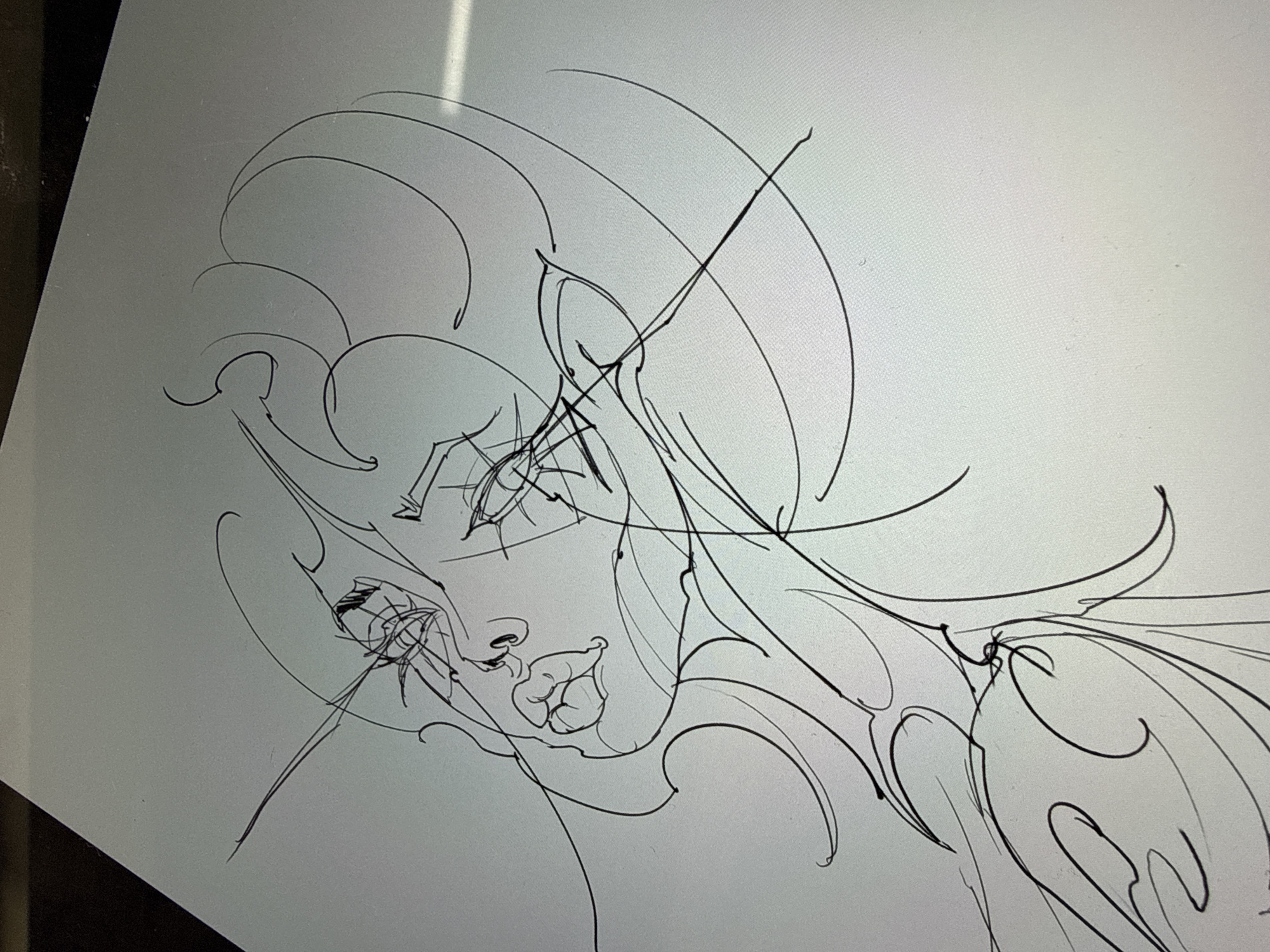 A black and white line drawing on a light-colored surface (likely a digital tablet or paper). The drawing depicts a stylized portrait of a woman with prominent features, including exaggerated lips, an arched eyebrow, and flowing hair or headdress elements. The style of the drawing is fluid and somewhat abstract, with expressive lines defining the subject. There is no indication that this scene is in Sofia, Bulgaria.