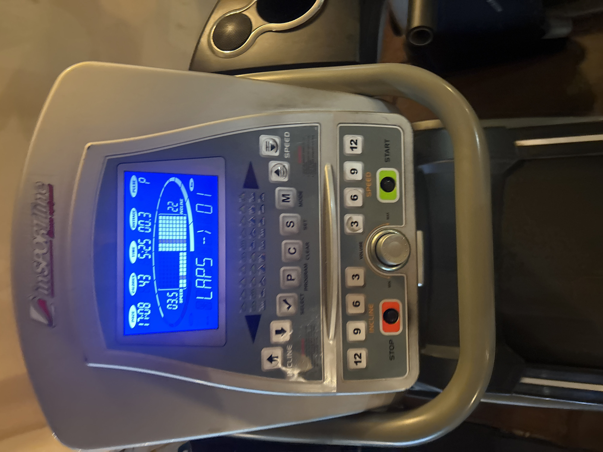 The image depicts a close-up view of the control panel of a treadmill, likely indoors. The panel features a blue digital display showing the time (17:08), calories burned (43), time elapsed (5:25), distance (00.3), speed (03.5), incline (22) and laps (01). Buttons are visible for speed, mode, incline, volume, program selection, and start/stop. The brand name "inSPORTline" is visible on the side of the control panel.