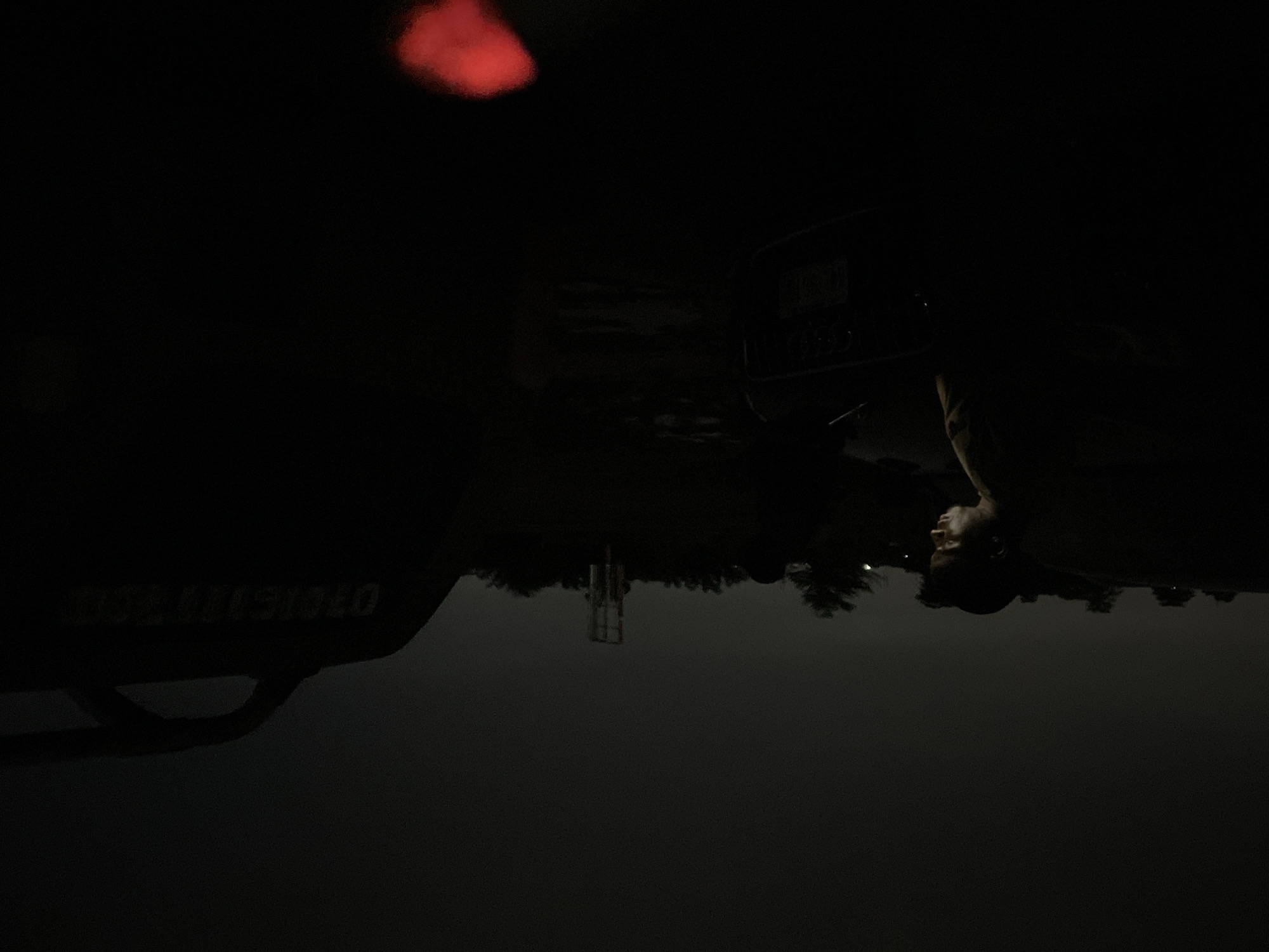 The image is taken at night in Abuja, Nigeria. A man is standing near a vehicle. The license plate of the vehicle is partially visible. A cell tower is visible in the background. A red light is visible overhead.