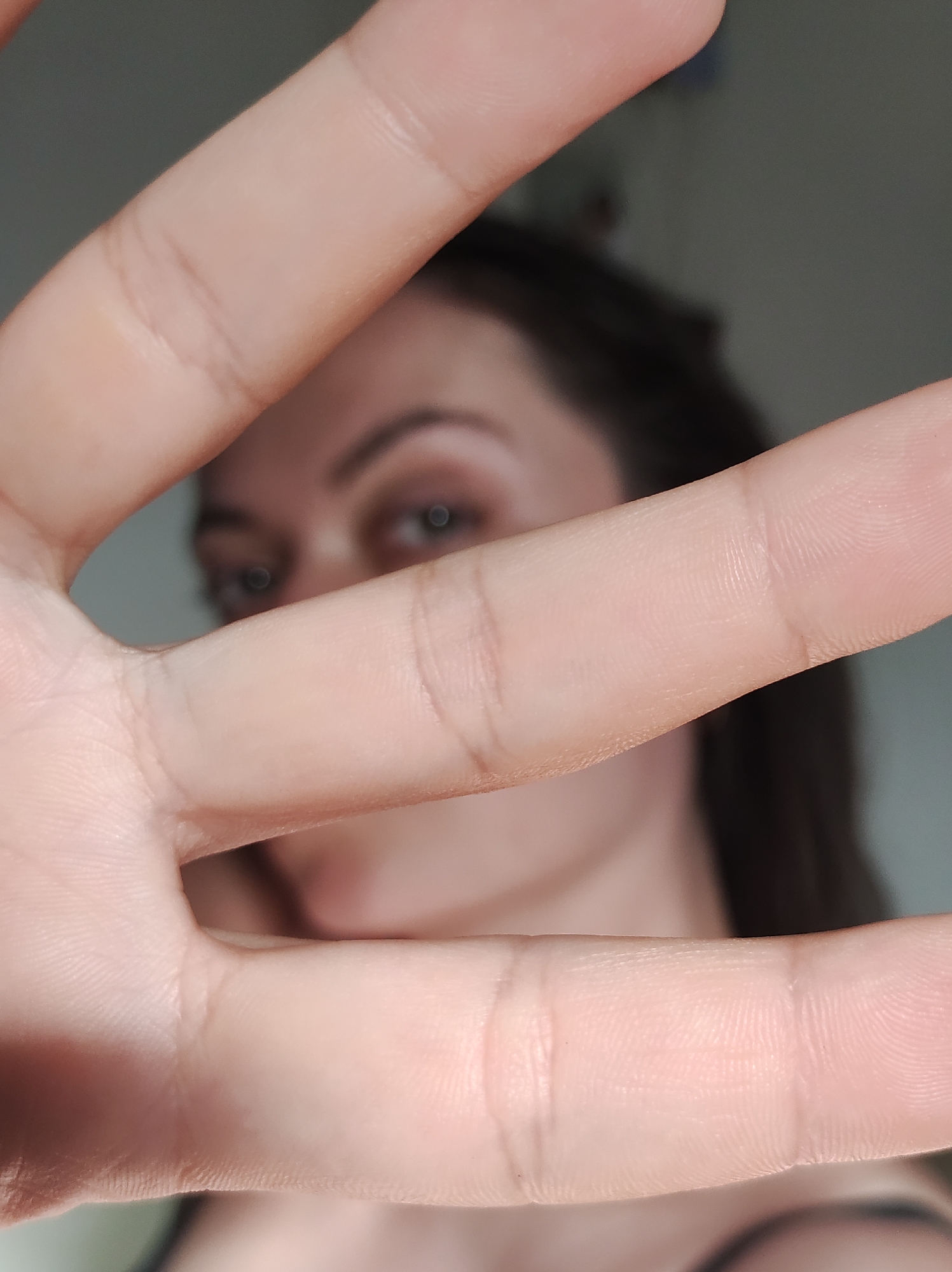 A photograph depicts a woman's face obscured by her hand held up close to the camera. Only her eyes are clearly visible through the gaps between her fingers. The location is unknown.