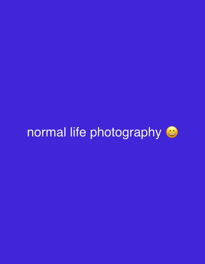 The image displays a uniform, solid royal blue background. Centered horizontally is the phrase "normal life photography" rendered in white, sans-serif text. Immediately to the right of "photography," a yellow emoji depicts a smiling face with closed, upturned eyes and an open mouth revealing upper teeth. This scene is situated in the city of Jos, Nigeria.