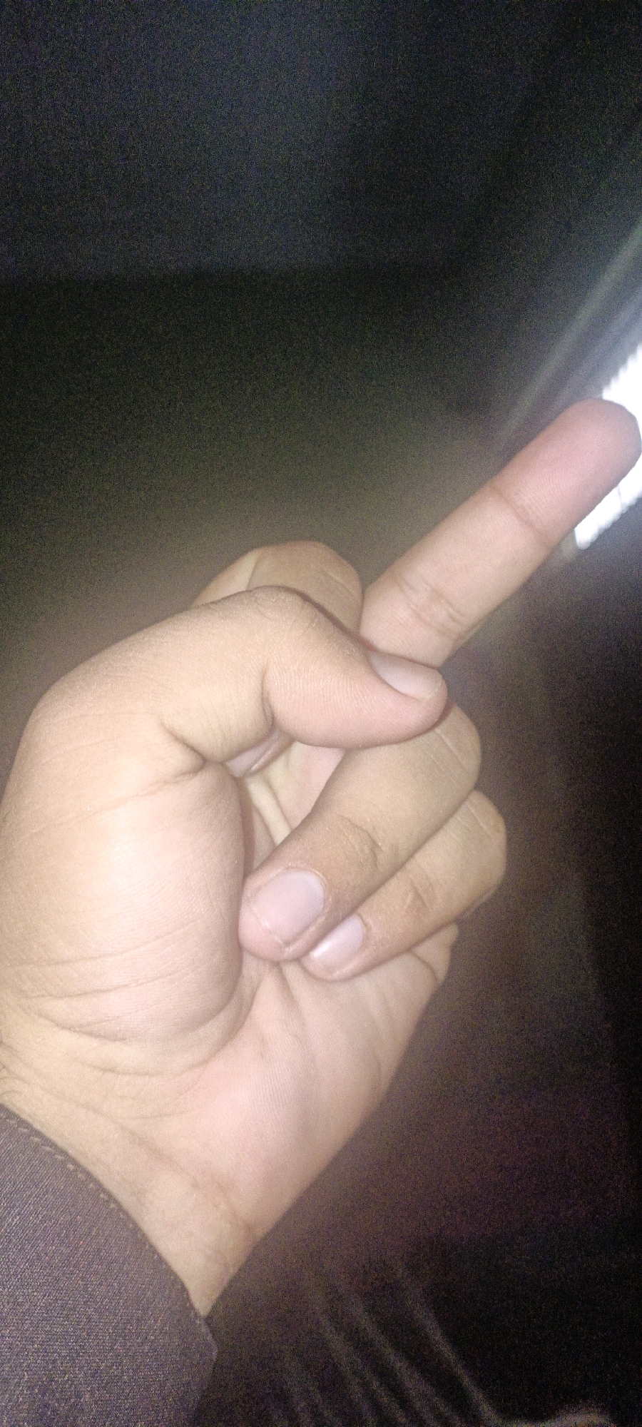 The image shows a close-up of a hand with the middle finger extended. The hand appears to be held up against a dark, textured background. Part of a sleeve or clothing is visible on the lower left of the frame. There is a light source to the right of the image, casting a glow on the fingers. The image quality is grainy and has low resolution, making it difficult to discern fine details. No specific location within CHAK NO.172 TDA, Pakistan can be identified from the visual information provided.