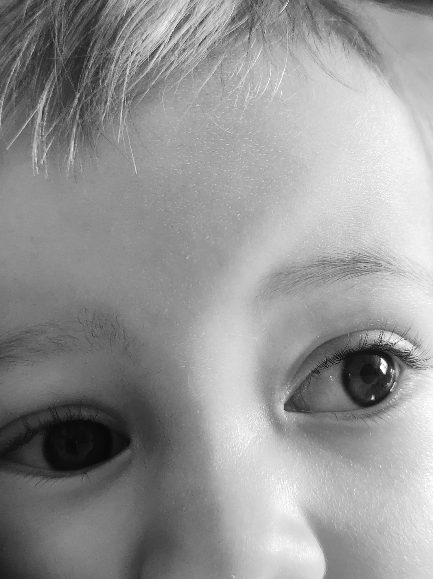 A close-up, black and white photograph shows a portion of a child's face. The focus is on the eyes, eyebrows, forehead, and part of the nose. The child's hair is visible at the top of the image. The eyes are dark and appear to be looking slightly to the side. The skin is smooth. There is no indication in the image about the location in the city of Фоки, Russia or any other information about the environment.