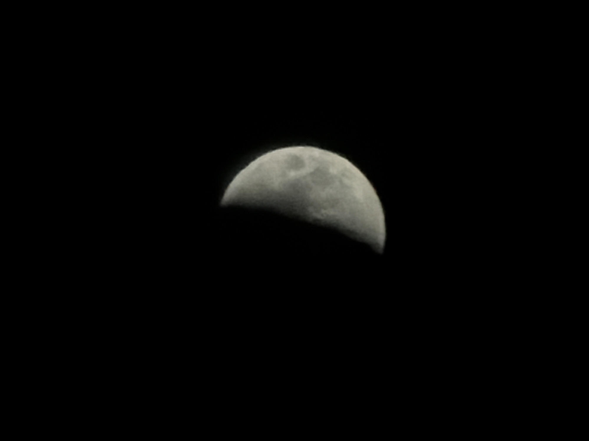 The image depicts a half-illuminated moon against a black sky. The moon's surface shows craters and texture. The location of Izhevsk, Russia, is not determinable from the image.