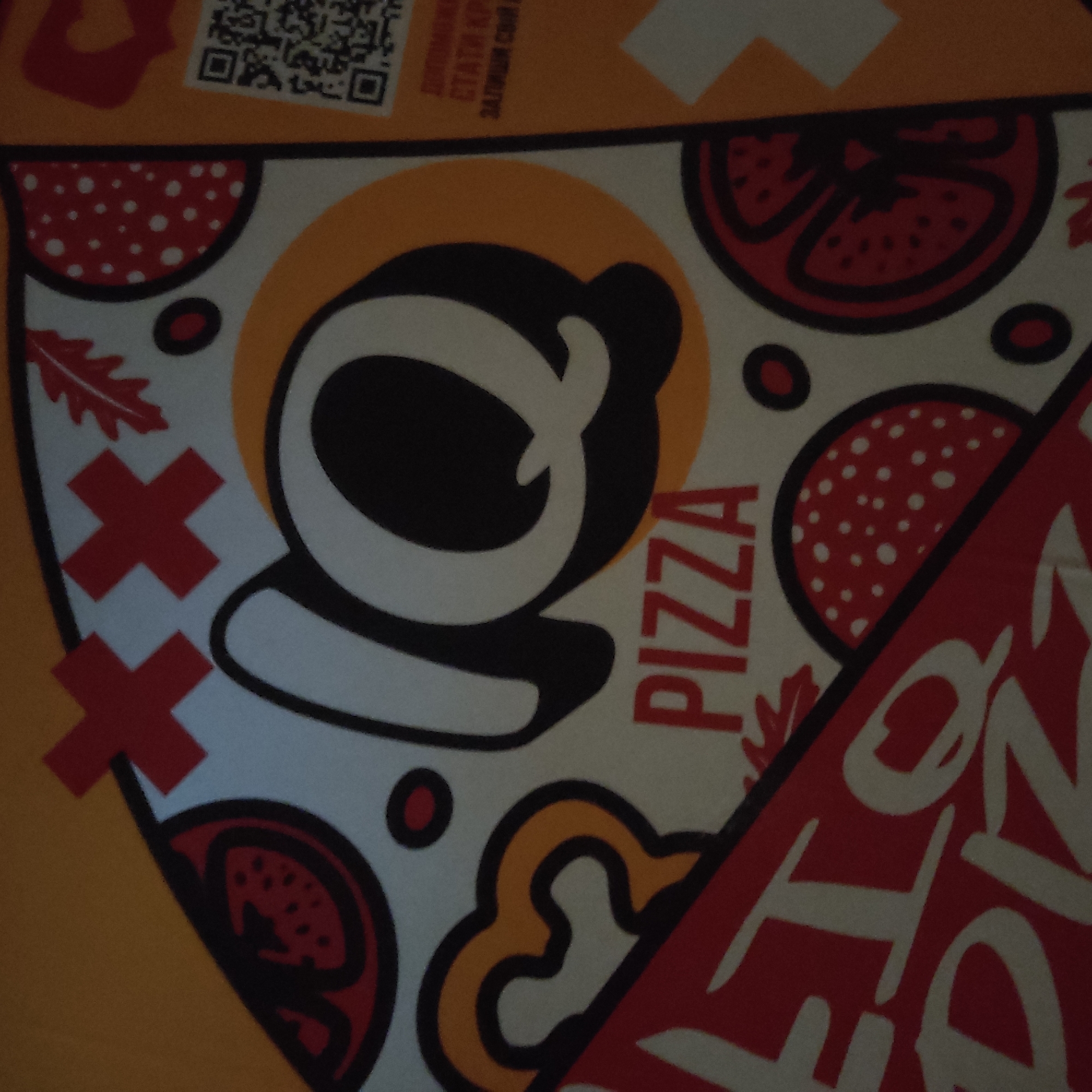 The image shows a close-up of a pizza box with a stylized, cartoonish design. The background is a bright yellow. Dominating the center is a large, white "Q" outlined in black, with a smaller "IQ" above it formed by red crosses. Below the "Q" is the word "PIZZA" in large, red, block letters. Various graphic elements, including red circular shapes with white dots (resembling pepperoni or sliced tomatoes), red tomato slices with black seeds, and a stylized yellow pepper shape, are scattered around the "Q" and "PIZZA" text. A red leaf-like shape is visible to the upper right of the "Q". The lower left of the image features a diagonal red band with white lettering that appears to say "ILTO PIZZA" in a stylized font. The upper right corner contains a QR code and some Ukrainian text. The image quality is low, with a slightly blurry appearance and muted colors. There are no people or discernible environmental context beyond the pizza box itself. The location is given as Unknown, Unknown.