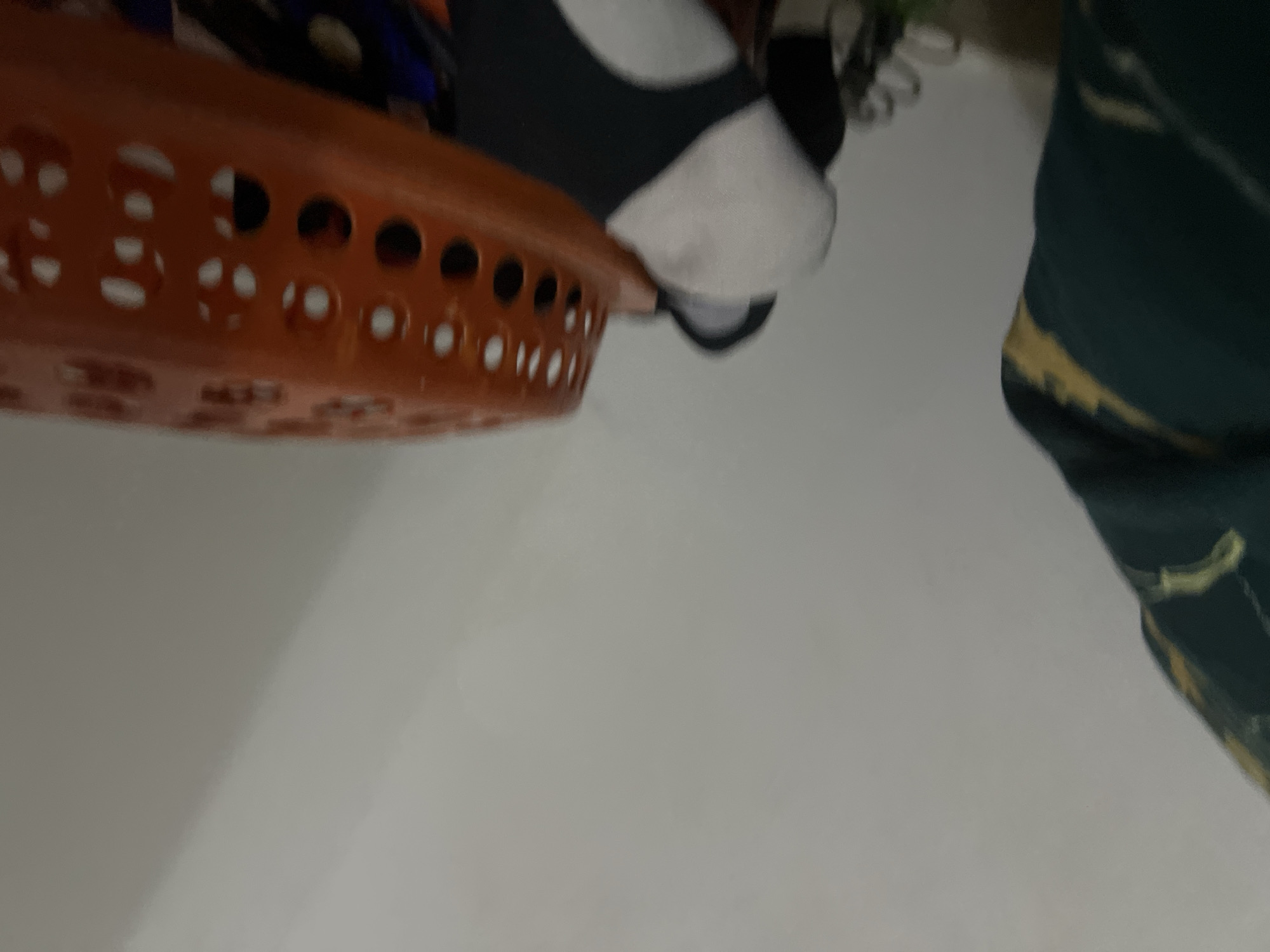 The image shows a close-up view of laundry, including a green and yellow patterned fabric on the left and an orange laundry basket filled with clothing on the right. The scene appears to be indoors, with a light-colored wall in the background. The lighting suggests it might be daytime, but the overall impression is of a cluttered domestic space. There are no visible people or indications of specific activities. The location in Howayi, Nigeria, is not discernible from the visual information provided in the image.