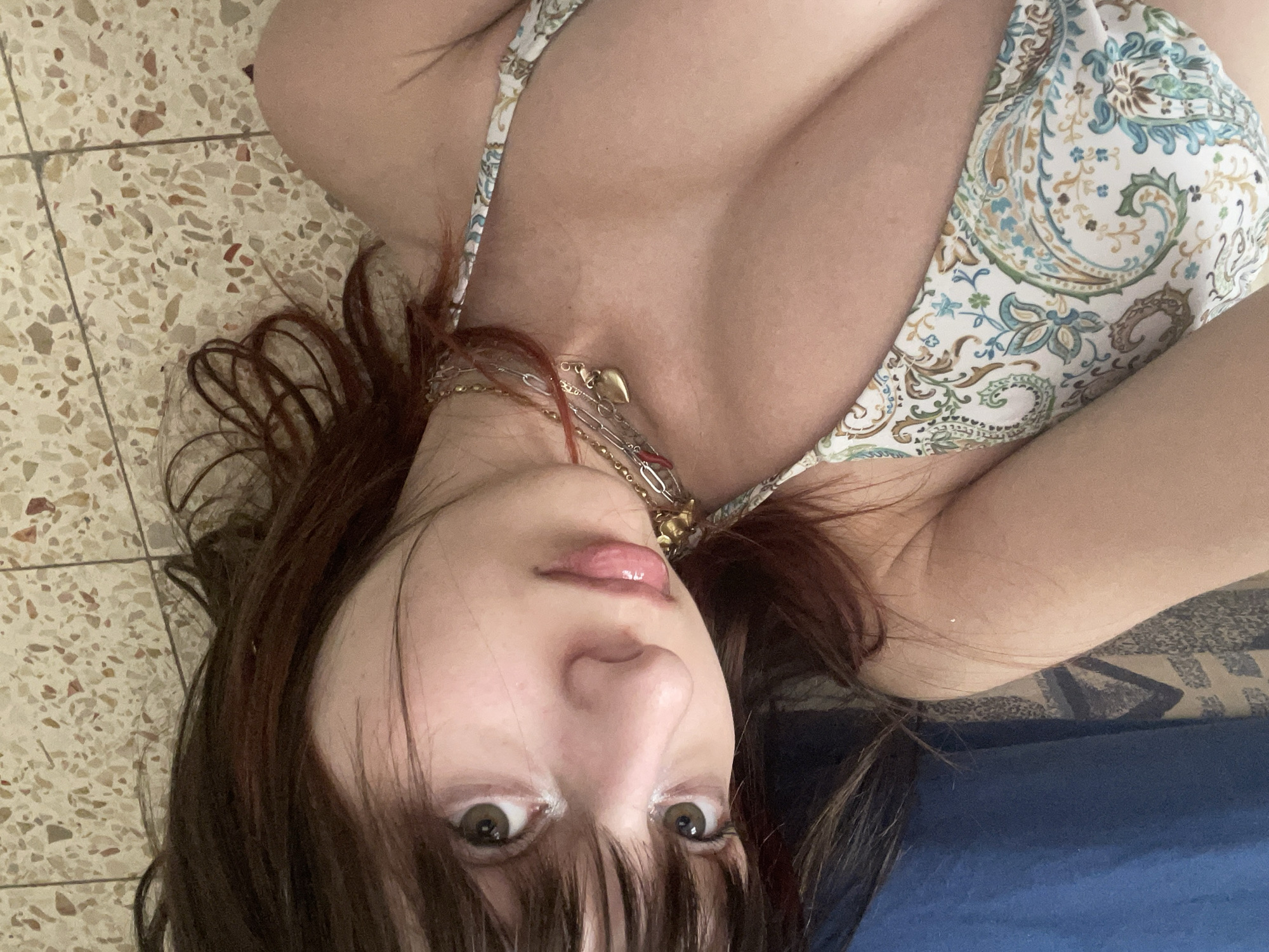 A woman with brown hair and light eyes lies on a blue surface next to a tile floor. She is wearing a patterned top and multiple necklaces. The location is not identifiable as Petah Tikva, Israel.