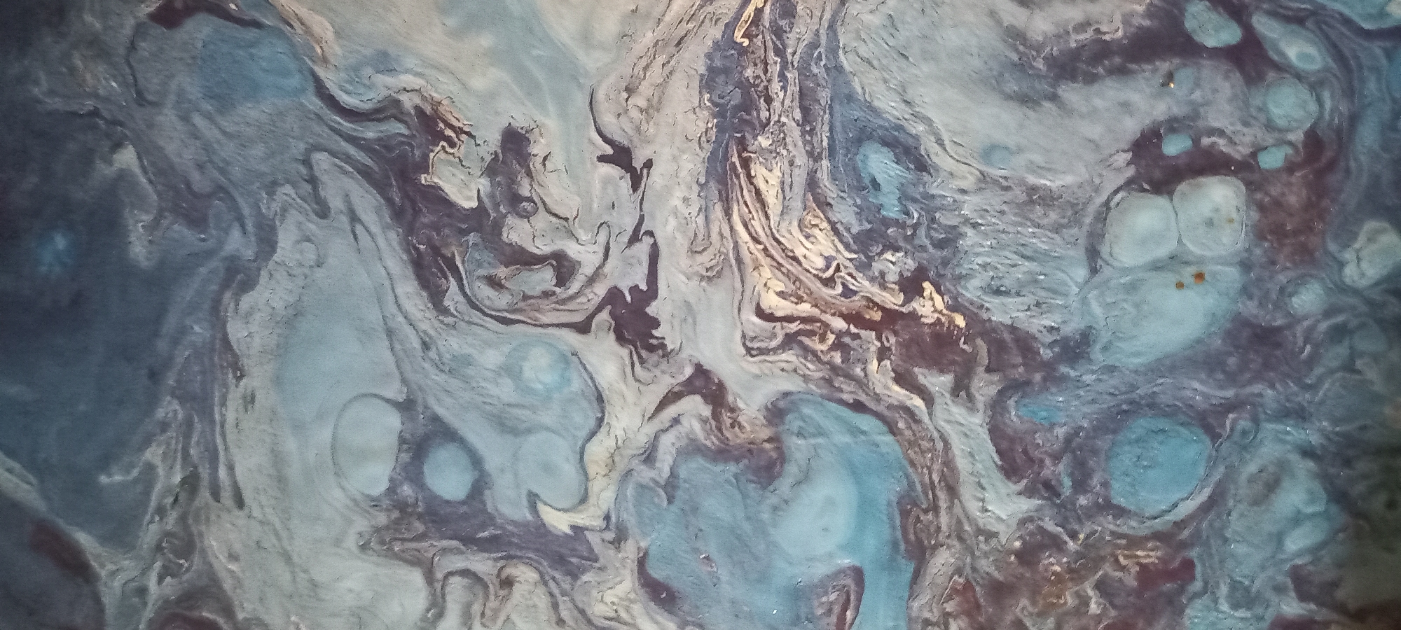The image shows an abstract painting with swirling patterns of blue, gray, and dark purple hues. The texture appears to be fluid, with areas of lighter and darker tones blending into each other. There are no discernible objects, people, or actions depicted. The painting does not provide any information that would allow for its location in the city of Kryvyi Rih, Ukraine, or any other specific location.