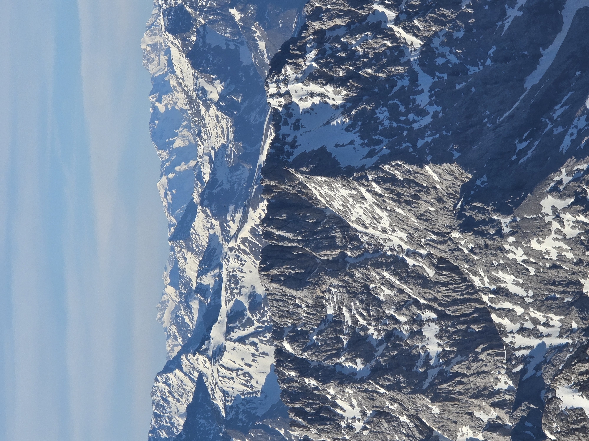 The image shows a mountain range, possibly the Wetterstein mountains, adjacent to a pale blue sky. The mountains are partially covered in snow. The image is oriented vertically, suggesting it may have been rotated from its original capture. Grainau, Germany is located in the Bavarian Alps at the foot of the Zugspitze.