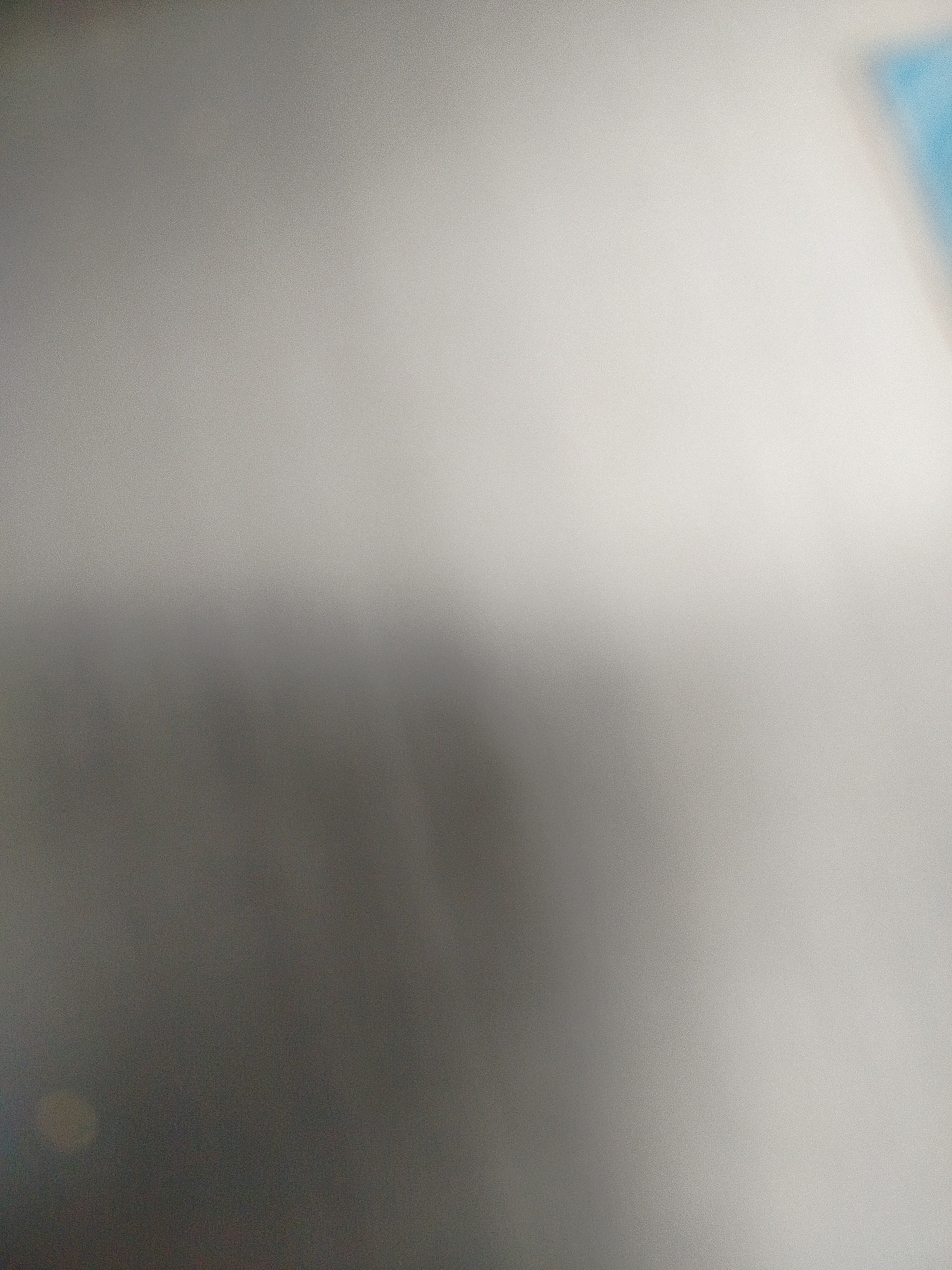 The image is blurry and out of focus. The predominant color is grey, transitioning from a darker shade in the lower left to a lighter shade towards the upper right. There is a hint of blue in the upper right corner. No specific details about Yerevan, Armenia, or any identifiable people, objects, or actions can be discerned from the image.