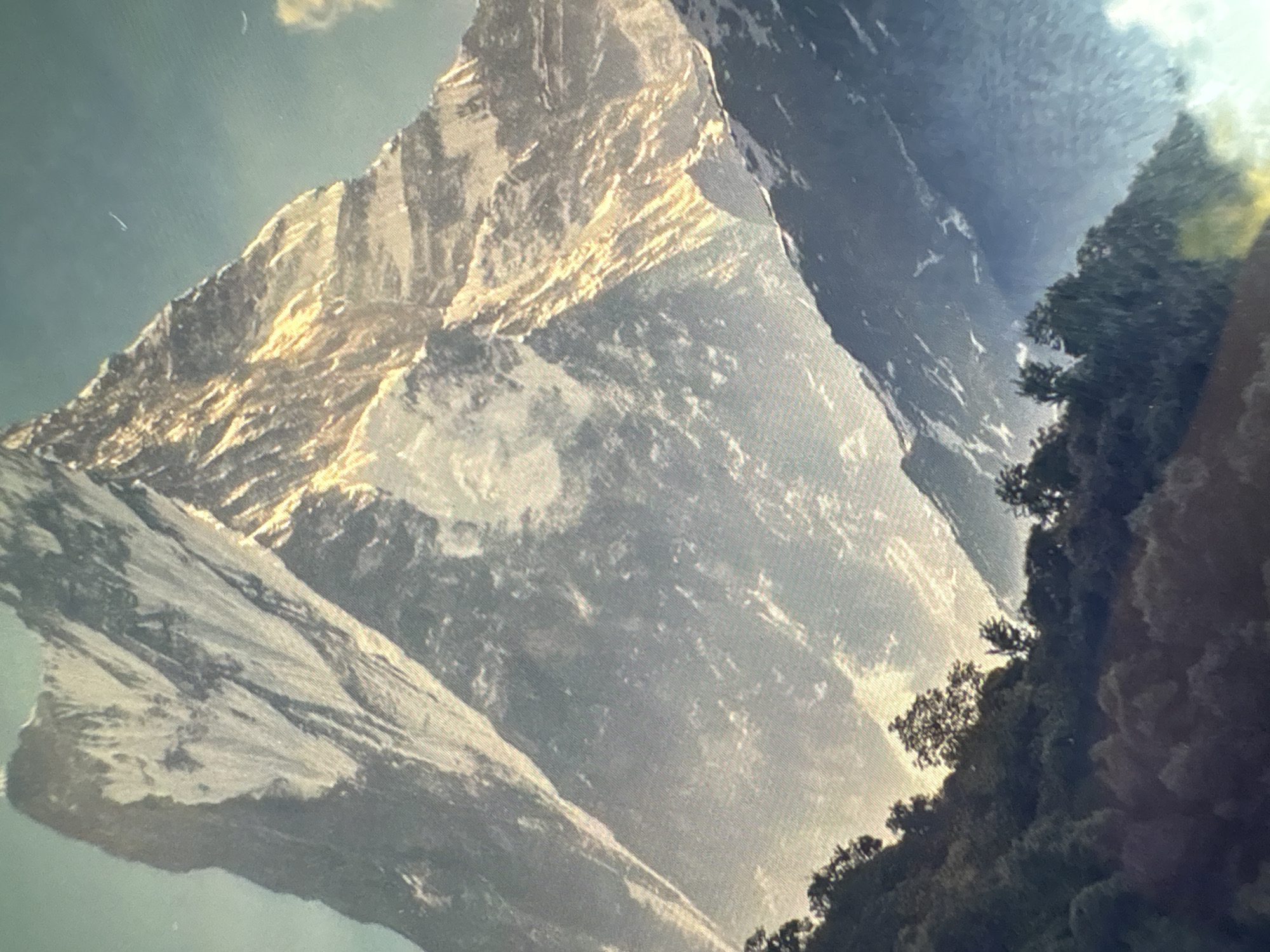 The image shows a mountain range with snow-capped peaks, appearing to be bathed in sunlight. A portion of the mountainside is covered with trees. The scene appears to depict a mountainous environment, though a specific location in Kukorevo, Bulgaria, cannot be confirmed based solely on the image.