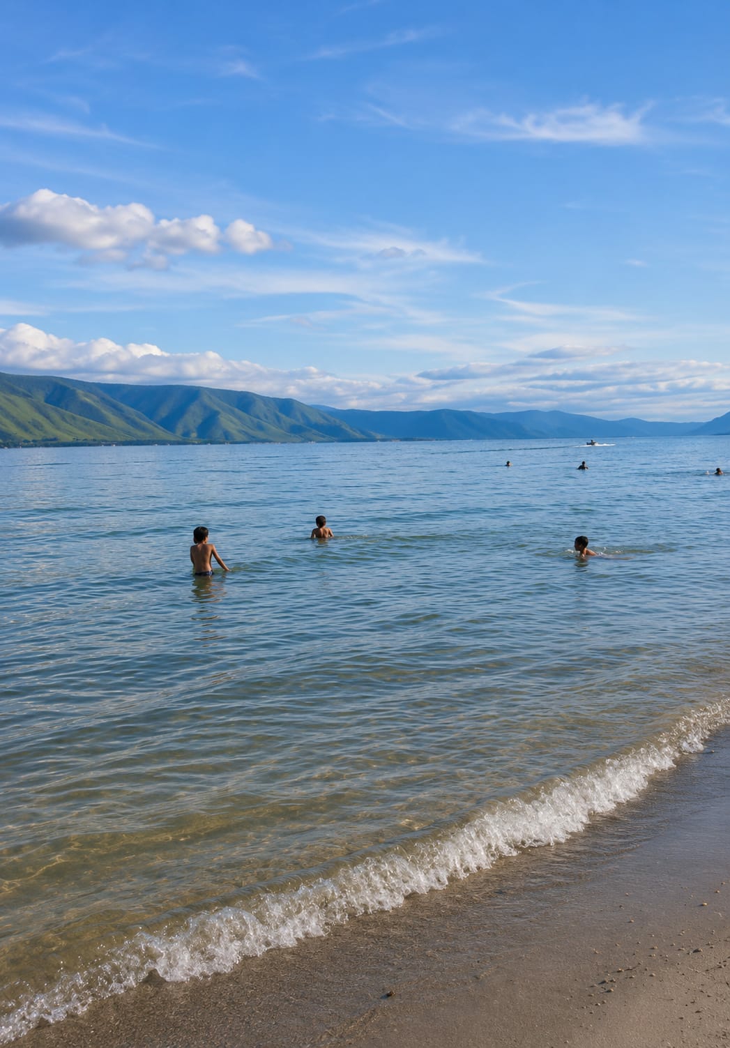 The image depicts a serene, natural landscape with a body of water and distant mountains. Several children are visible in the water, with some wading and others swimming. The water is clear, with gentle waves lapping at the sandy shore in the foreground. The sky is a bright blue, dotted with fluffy white clouds. Mountains with lush green slopes rise in the background, forming a picturesque backdrop. A small boat is visible in the distance on the water. The scene appears to be a tranquil day at a lake or sea, likely in a location like Situngkir, Indonesia, known for its natural beauty.