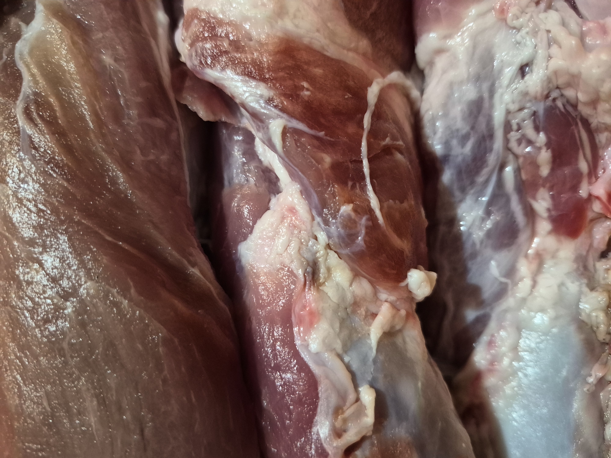 The image is a close-up, high-angle shot of raw meat. The meat is a reddish-pink color with visible marbling and white fatty tissue. The texture appears moist and slightly glistening. The lighting highlights the different layers and textures of the meat. There are no people, animals, or the city of Uglegorsk, Russia visible in the image.