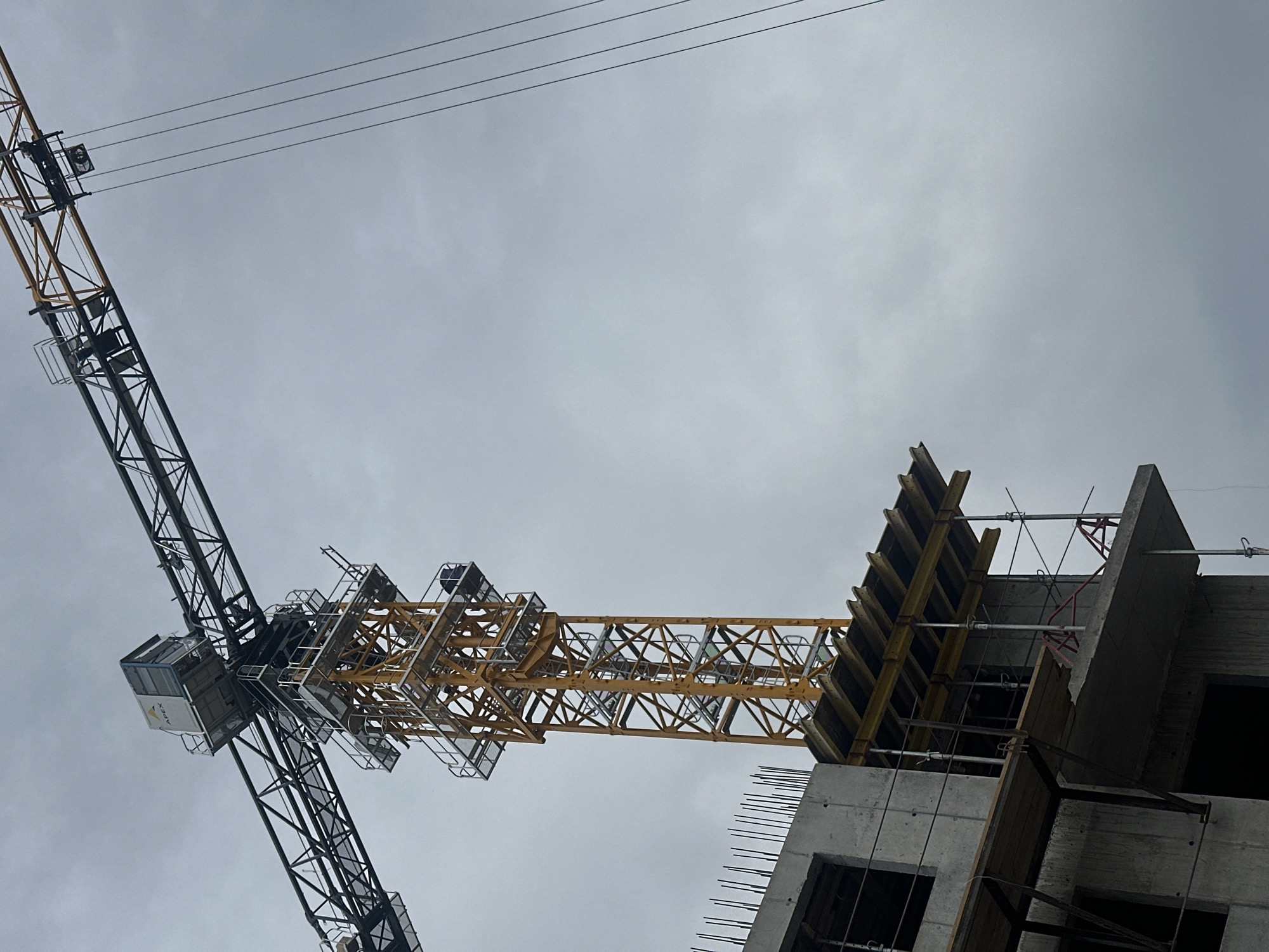 The image shows a construction site in Khabarovsk, Russia. A crane is attached to a partially constructed concrete building. The sky is overcast. There are power lines in the upper portion of the image. The building is under construction, with wooden forms attached to the concrete structure, and rebar visible. No people are visible in the image.