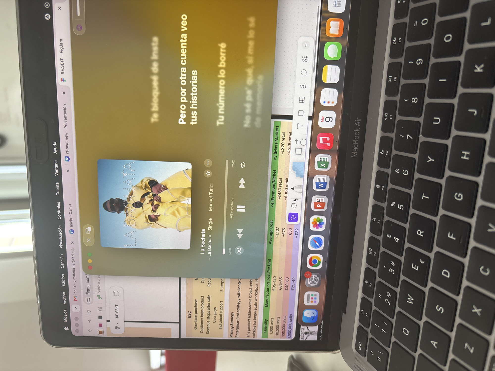 This is a close-up, eye-level shot of a silver MacBook Air laptop computer with its screen illuminated, displaying multiple open browser tabs and an application. The laptop is placed on a dark surface, likely a desk, and the keyboard is visible in the foreground. The screen shows a Spotify music player interface with album art featuring a man in a yellow outfit, song title "La Bachata," and playback controls. Adjacent to the music player, other browser tabs are visible, including "Inbox - c.mataforner@ied.edu," "Inicio - Canva," and "re.seat new - Presentación," as well as a Figma tab. A table with pricing information, including "Quantity" and "Manufacturing Cost Per Unit," is partially visible on the left side of the screen. The laptop's operating system dock is also visible at the bottom of the screen, showing various application icons. The background is out of focus, showing hints of interior lighting. There are no external environmental cues to suggest a specific location within Milan, Italy. The image captures a moment of digital activity on the laptop.