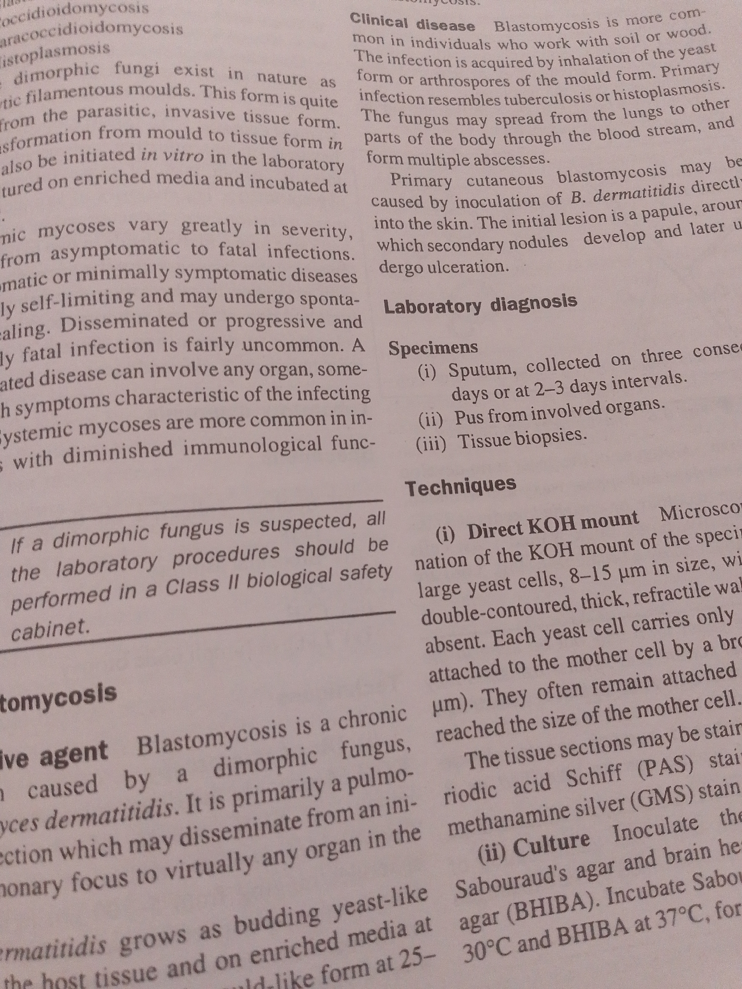 The image displays a close-up view of a book or document page, focusing on medical or scientific text. There are no people, objects, or a scene in the traditional sense. The setting is implied to be a place where such documents are studied or produced, such as a library, office, or laboratory.
The activity taking place is the presentation of information through printed text. The notable details are the technical terms related to mycology and infectious diseases, including "coccidioidomycosis," "histoplasmosis," "Blastomycosis," and "yeast cells." The text discusses clinical disease, laboratory diagnosis, and techniques such as KOH mounts and cultures. Specific references to "Sputum," "Pus from involved organs," and "Tissue biopsies" suggest diagnostic procedures. The mention of incubation temperatures like "37°C" and media like "Sabouraud's agar" further points to a biological or medical context.
Visible text includes headings like "Clinical disease," "Laboratory diagnosis," "Specimens," and "Techniques." The body of the text elaborates on the causes, transmission, symptoms, and diagnostic methods for blastomycosis. The location context provided ("Jauro Yinu, Nigeria") is not evident from the image itself but is an external piece of information. There are no indications of time of day, weather, or emotions as the image solely contains text.