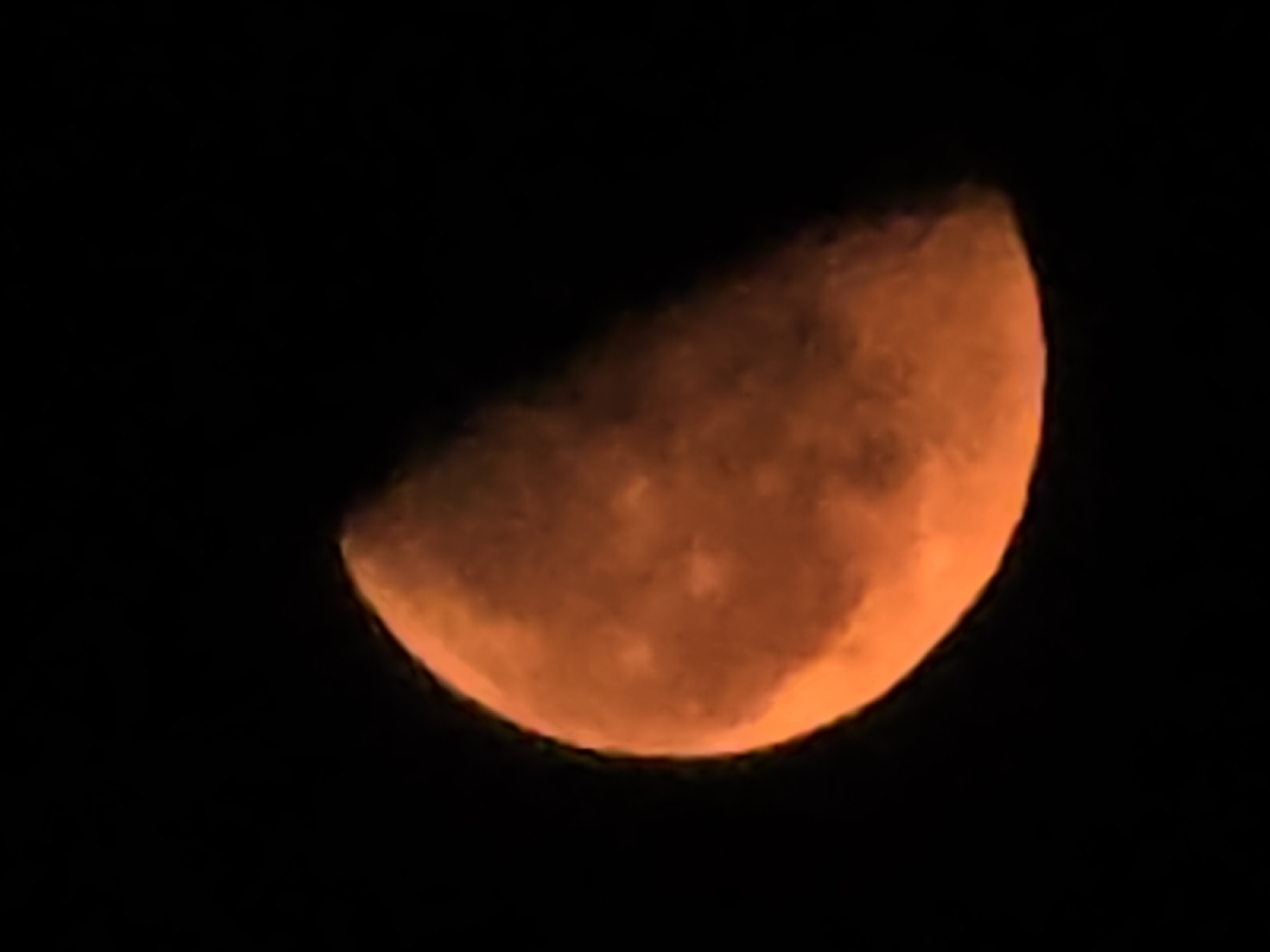 A crescent moon, with an orange hue, is visible against a black sky. The moon's surface shows subtle variations in texture and shading. The image does not contain any information about the city of Yambol, Bulgaria.