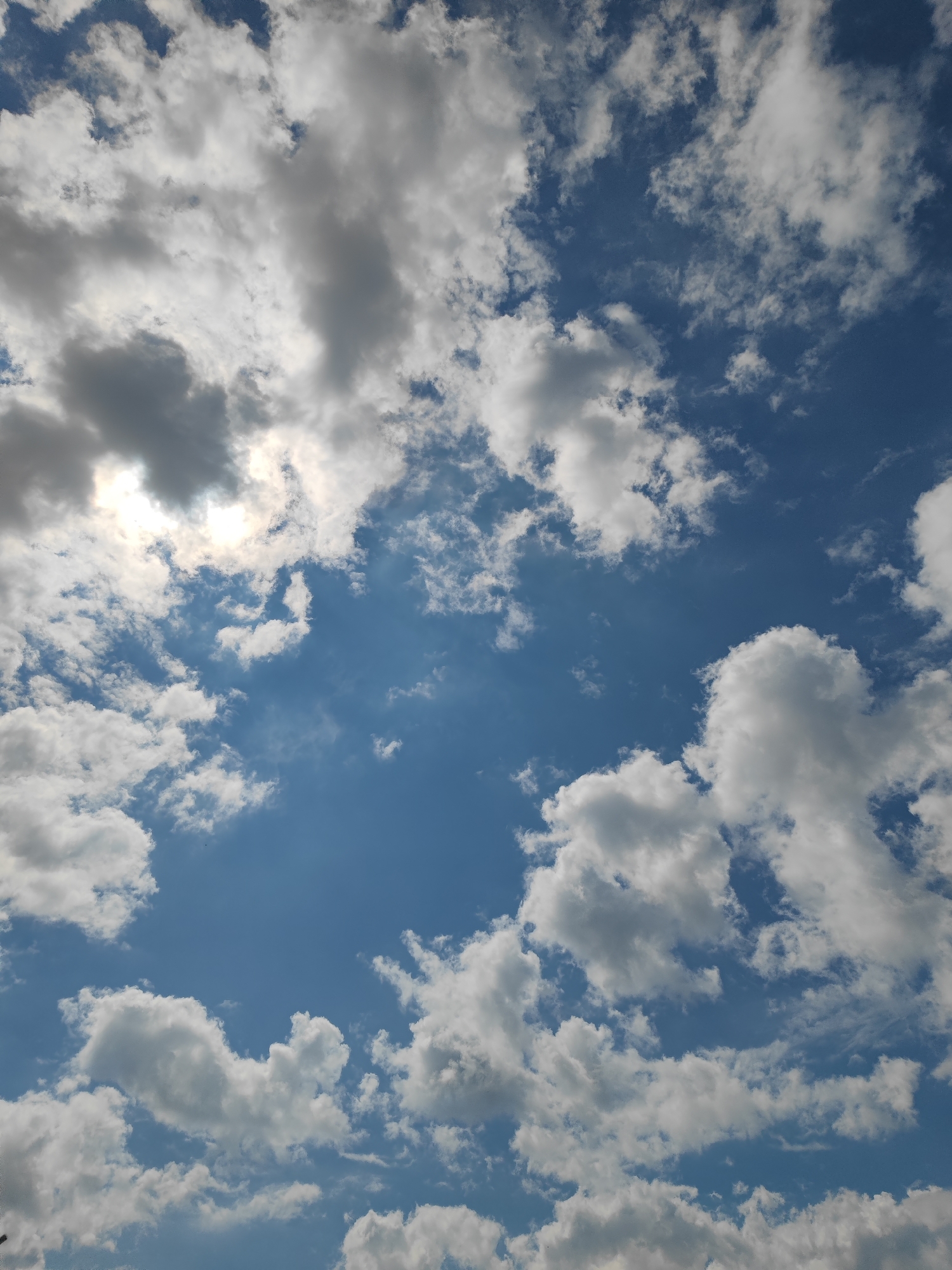 The image shows a sky with scattered white and gray clouds against a blue backdrop. The sun is partially obscured by clouds in the upper left portion. The location, Sennoy, Russia, cannot be determined from the visual information provided. There are no discernible people, subjects, objects, actions, or interactions within the frame, only the sky and clouds are visible.
