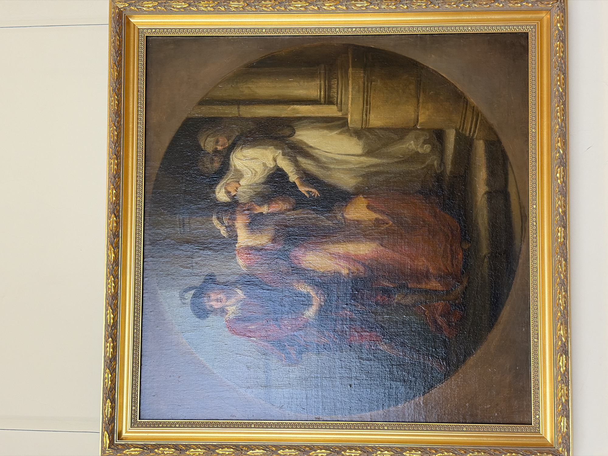 A framed oil painting depicts a dramatic scene within a dark, vaguely defined interior setting. The painting is set within an oval-shaped area surrounded by a dark background.
The primary figures include a woman in a white dress with a head covering, seemingly collapsing or dead, and another woman in a similar white garment who is supporting her. Below, a man with a hat is possibly looking on or involved. These figures are depicted with dark colors, suggesting drama. The presence of what seems to be a column suggests a formal, possibly architectural backdrop, and the overall composition implies a tragic or emotional event.
The painting is located in the city of Saint Petersburg, Russia.