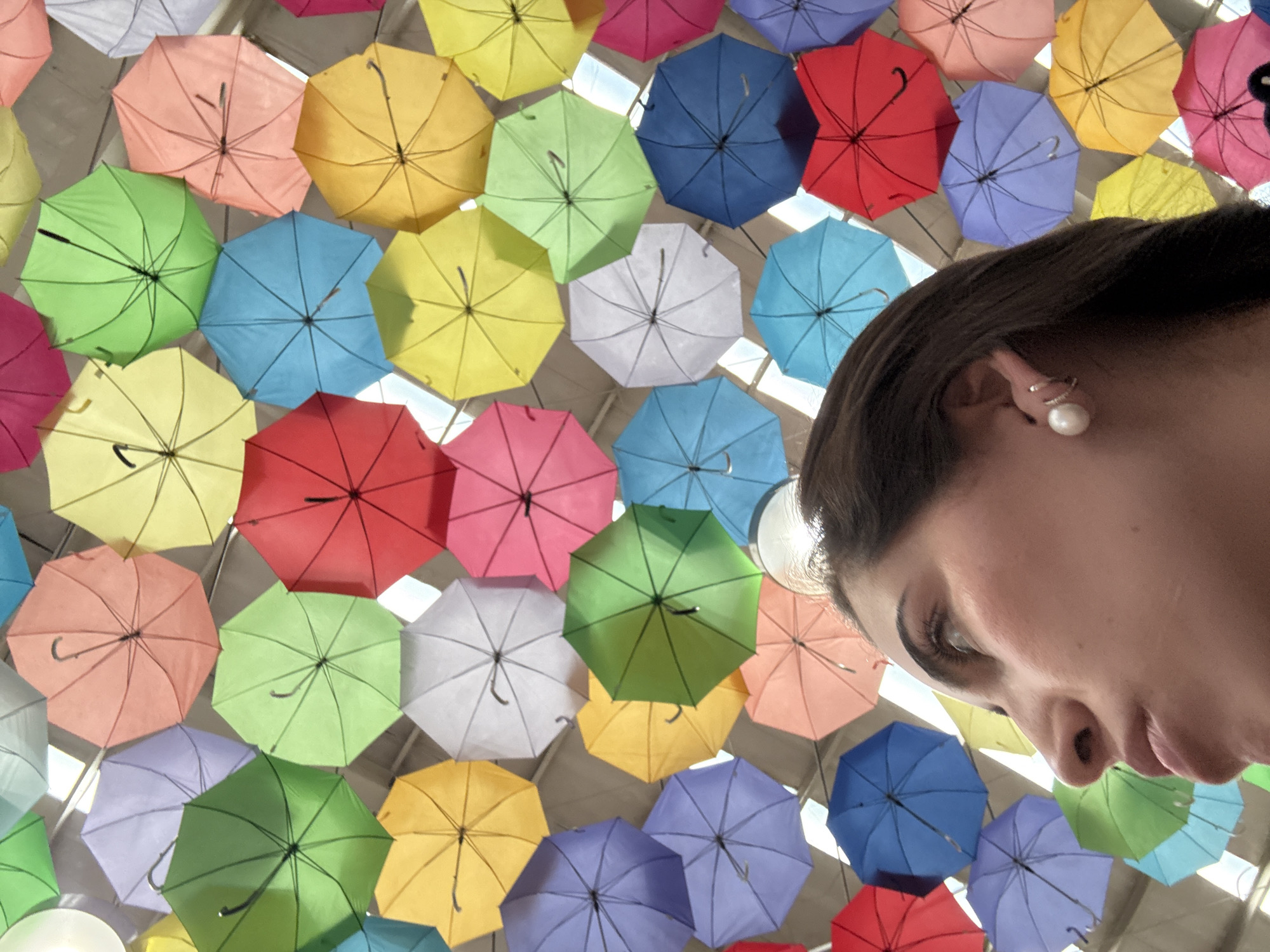 A woman is looking down at the camera, with a display of colorful umbrellas above her. The location is San Francisco Ocotlán (Ocotlán), Mexico.