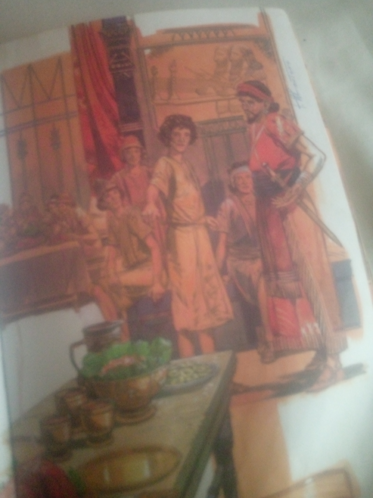 This image depicts an indoor scene with several people dressed in what appears to be historical or theatrical attire. Two prominent figures stand near the center, one wearing a red tunic and headdress, with a sword at his side, and another in a pale, patterned tunic. To their left, other individuals are visible, some in lighter-colored garments. The background suggests an opulent setting with red drapes and elaborate wall decorations that resemble ancient murals or tapestries. In the foreground, a table is laden with what seem to be food items, including a bowl of salad and other dishes.
The scene appears to be a gathering or a moment of historical reenactment. The lighting is warm and suggests an indoor setting, possibly a banquet or a royal court. The overall mood seems composed and formal. There are no clear indicators of the time of day or weather. The image's context is Jauro Yinu, Nigeria, which could imply a cultural or historical representation specific to that region, though the attire and setting do not immediately suggest a Nigerian context. There is faint, illegible text present on the right side of the image, likely a signature or title.