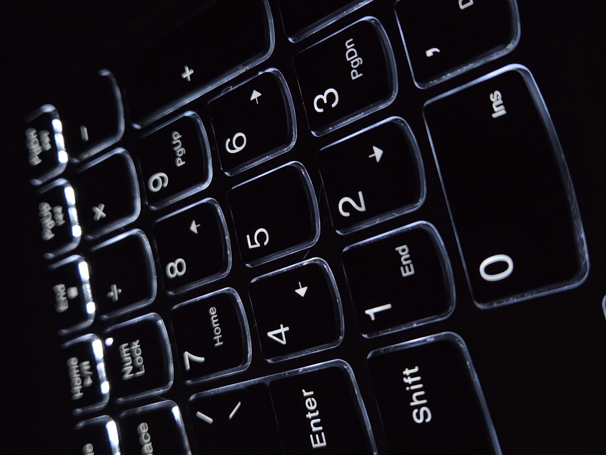 The image shows a close-up view of a laptop keyboard, focusing on the numeric keypad area. The keys are backlit with white illumination, highlighting the numbers and symbols. The keys are arranged in a typical numeric keypad layout, featuring numbers 0-9, along with mathematical symbols (+, -, *, /), and function keys (Num Lock, Home, PgUp, PgDn, End, Ins, Enter, Shift). The background is dark, emphasizing the illuminated keys. The environment is unknown, and there are no people visible in the image.