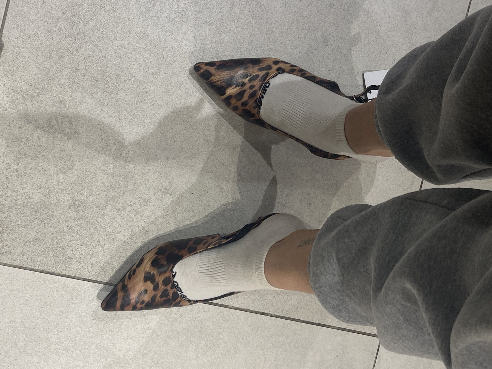 A person wearing gray sweatpants and white socks is posing with leopard print pointed-toe heels on a light gray tiled floor. The location is undetermined and there's no clear evidence to suggest it is in Kommunarka, Russia.