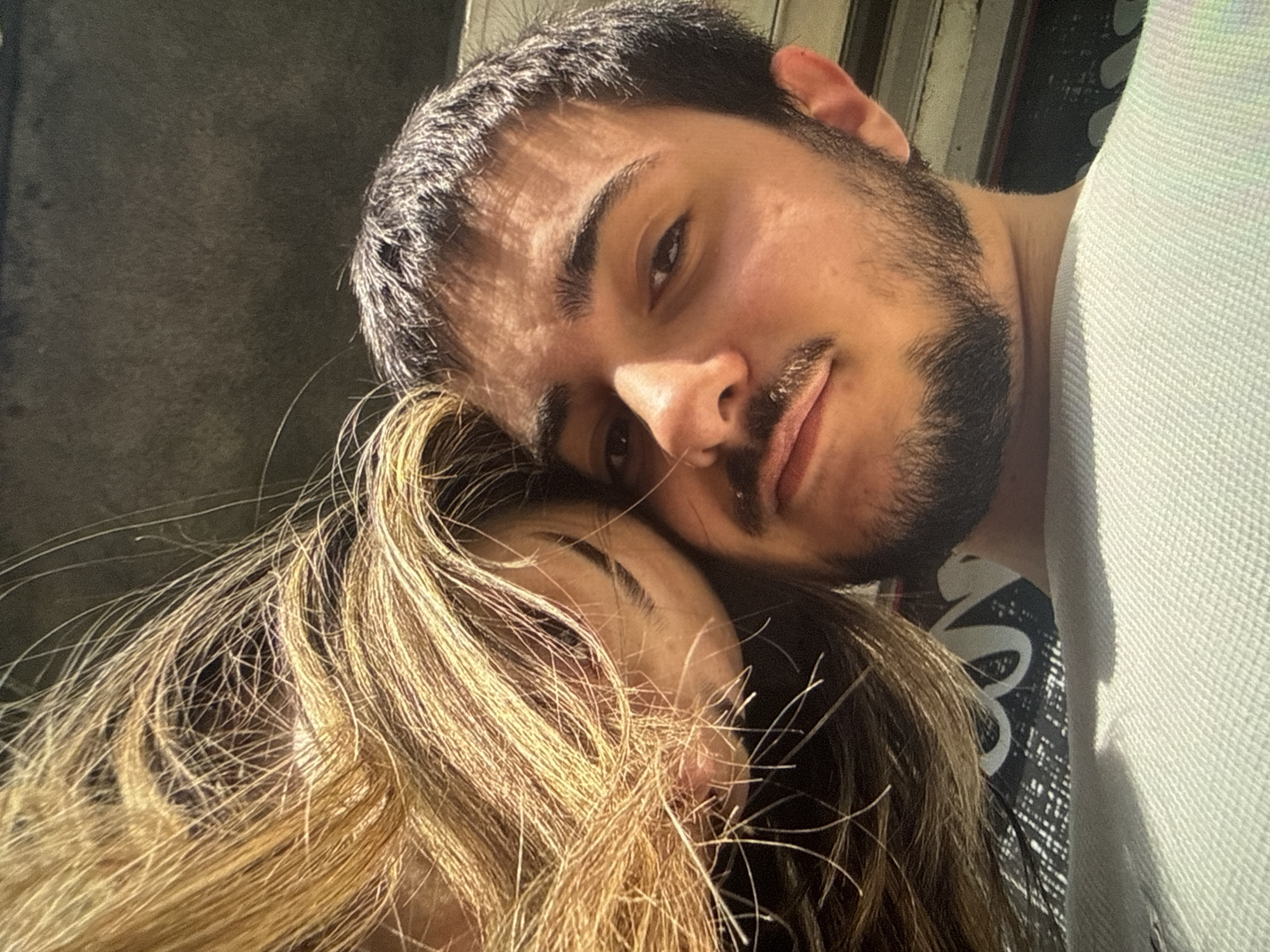 A man and a woman are posed closely together for a photograph. The man has dark hair and a dark beard. The woman has blond hair. The location is unknown, and there is no clear indication of Sofia, Bulgaria.