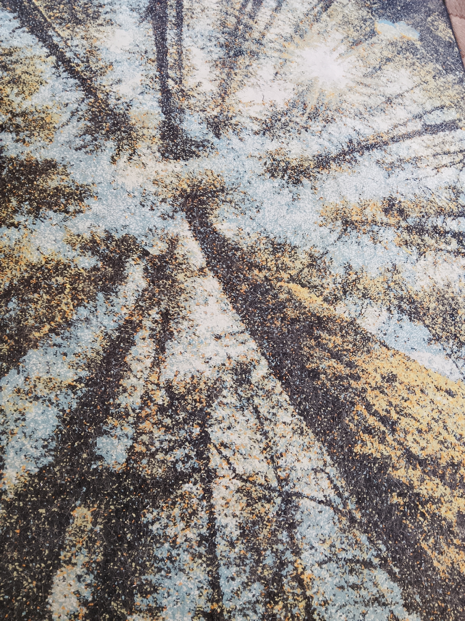 The image shows a close-up, abstract view of tree trunks and a canopy, as if looking up from the forest floor. The trunks are dark, vertical elements against a background of textured sky and foliage rendered in shades of light blue, yellow, and white. The overall impression is one of looking through dense trees towards a bright sky, possibly on an overcast or misty day. There are no people, animals, or identifiable structures in the image. It is not possible to determine the specific location within Abakan, Russia, based solely on this abstract depiction of a forest canopy.