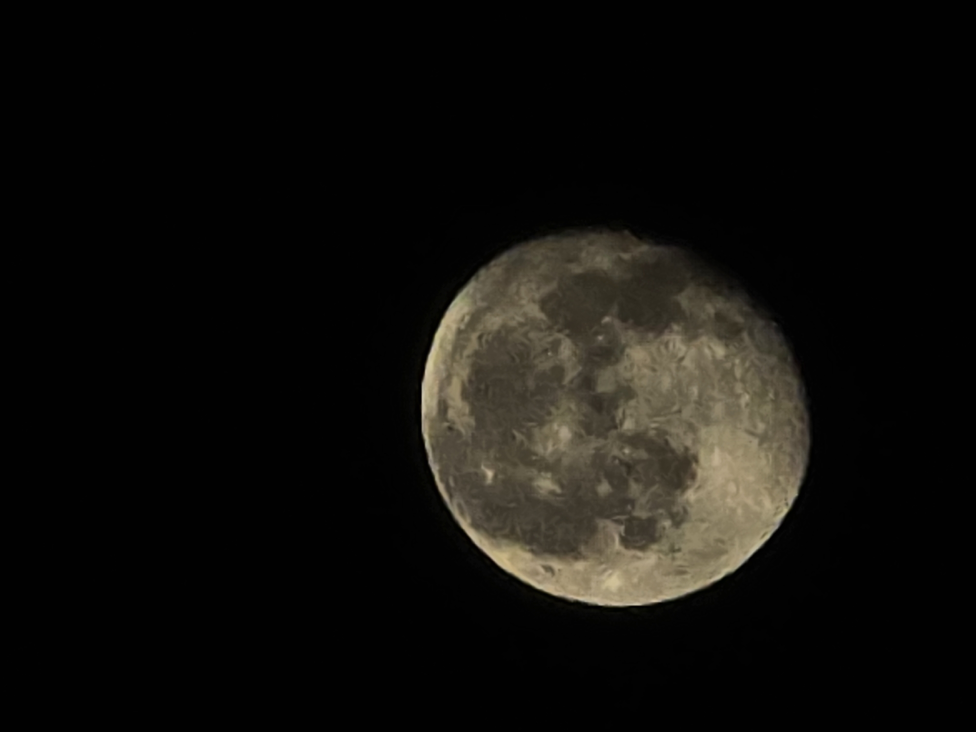 A full moon is visible against a black sky. The moon's surface displays variations in color and texture, suggesting craters and other geological features. The image is a close-up shot, with the moon occupying the lower right portion of the frame. There is no discernible location in the city of Yambol, Bulgaria, or any other specific geographical information present in the image.