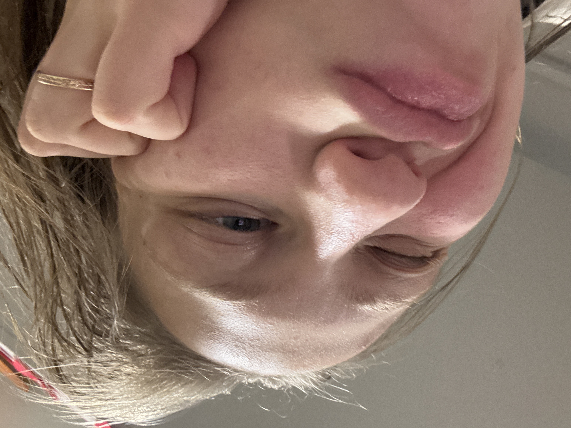 A close-up, angled selfie shows a fair-skinned person with blonde hair. The person's right eye is partially closed in a wink. They have a ring on a finger that is being used to push the skin of their face. The person is looking at the camera. The background is out of focus and appears to be a plain, light-colored surface. There is no information to suggest the image was taken in Perm, Russia.