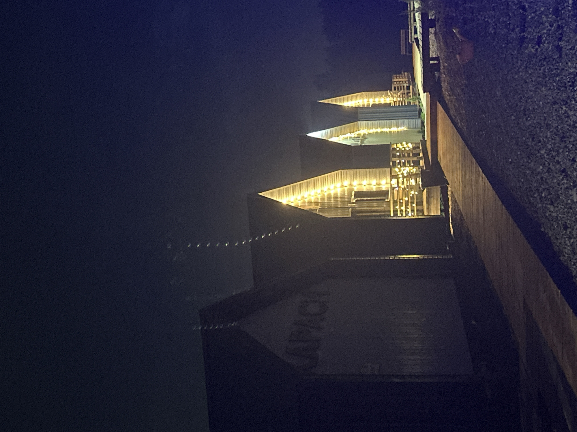 The image shows a building at night. A sign reading "LAVACH" is visible on the side of the building. Above, there are several levels with lights. To the right is a wall. The location is in Pirogovo, Russia.