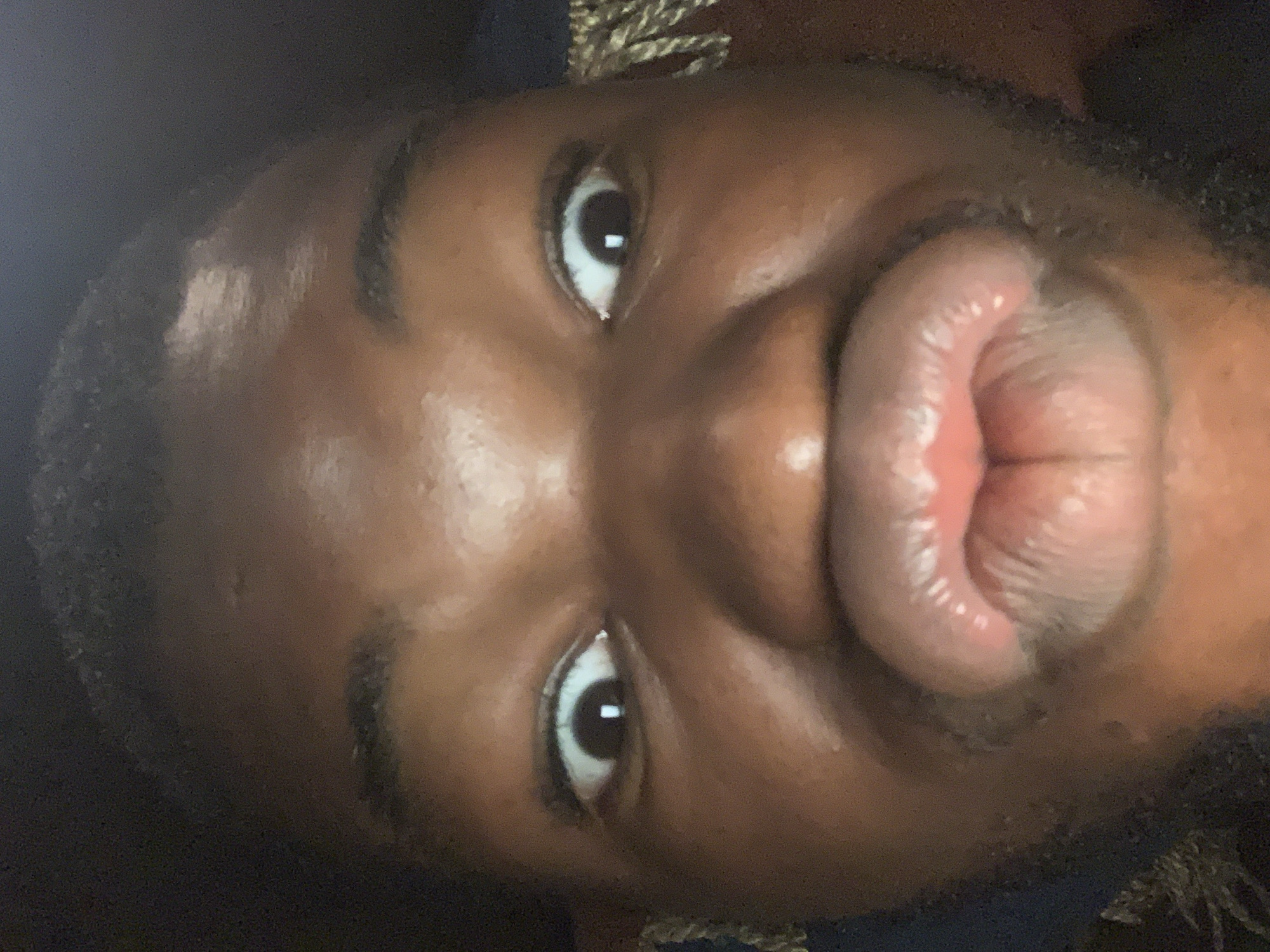 A close-up, rotated image shows a person with dark skin puckering their lips. The person has wide eyes and thick eyebrows. The image quality is slightly blurry and the lighting is bright on the face. There is no indication in the image that this photo was taken in Onitsha, Nigeria.
