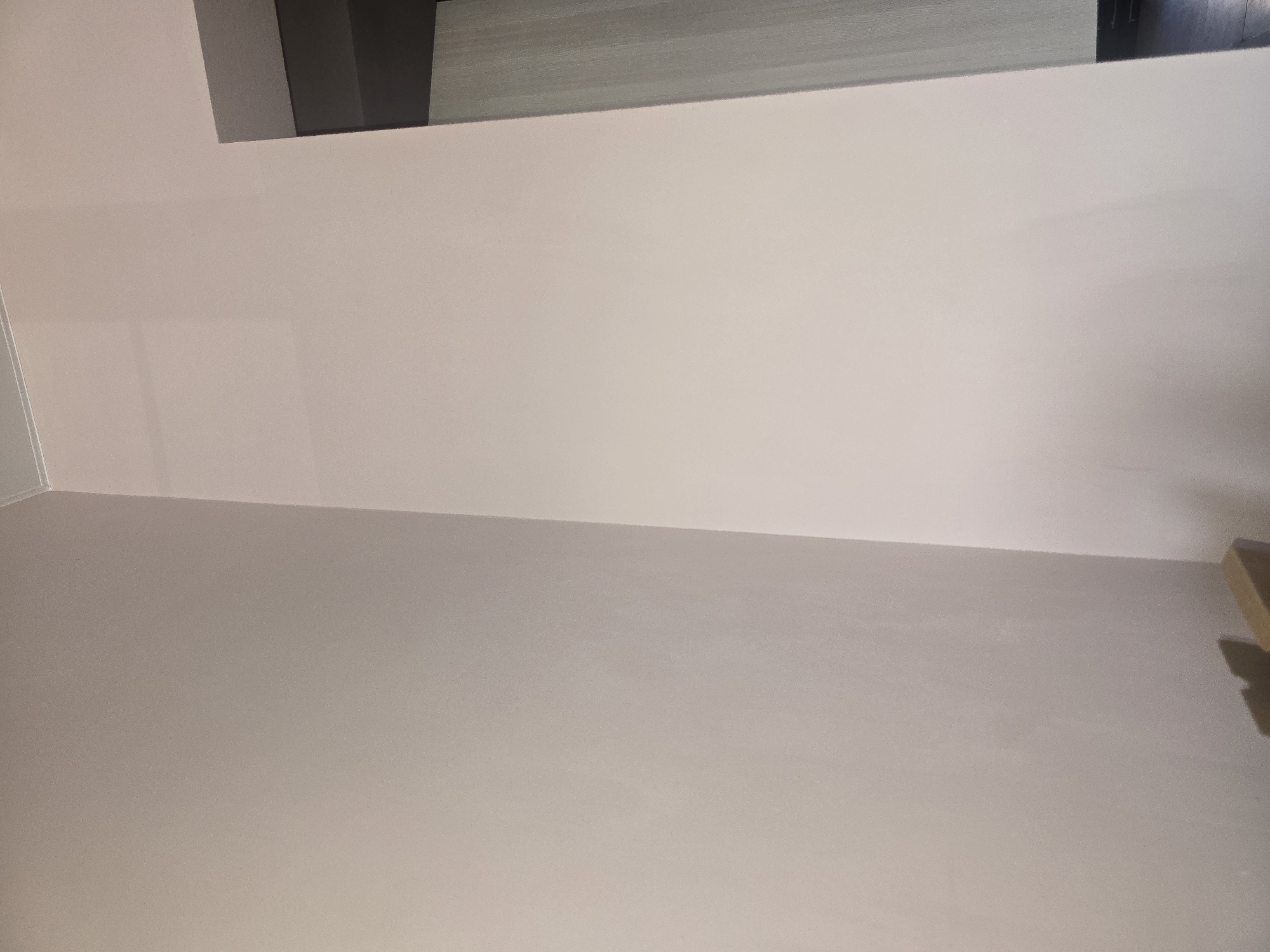 A corner of a room with two walls painted a light, neutral color. The walls meet at a right angle. The ceiling is visible at the top, with a thin white trim. To the right of the image, a doorway is partially visible, leading into a space with a patterned wall and a dark floor. There are no people or significant objects in the frame, creating a minimalist and clean aesthetic. The location in Ulan-Ude, Russia, is not discernible from the visual information provided in the image.