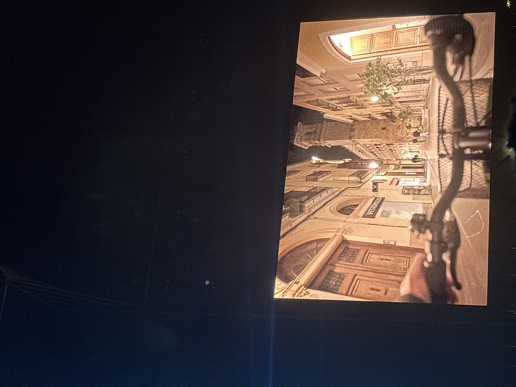 The image shows a screen displaying a rotated photograph of a European city street. The street features buildings with arched windows and wooden doors. Signage is visible, including the name "WESTOPAZZO." The city appears to be well-lit with street lamps and lights from within the buildings. A street lamp is visible. The location shown is unknown. The location in the city of Cunit, Spain is unknown.