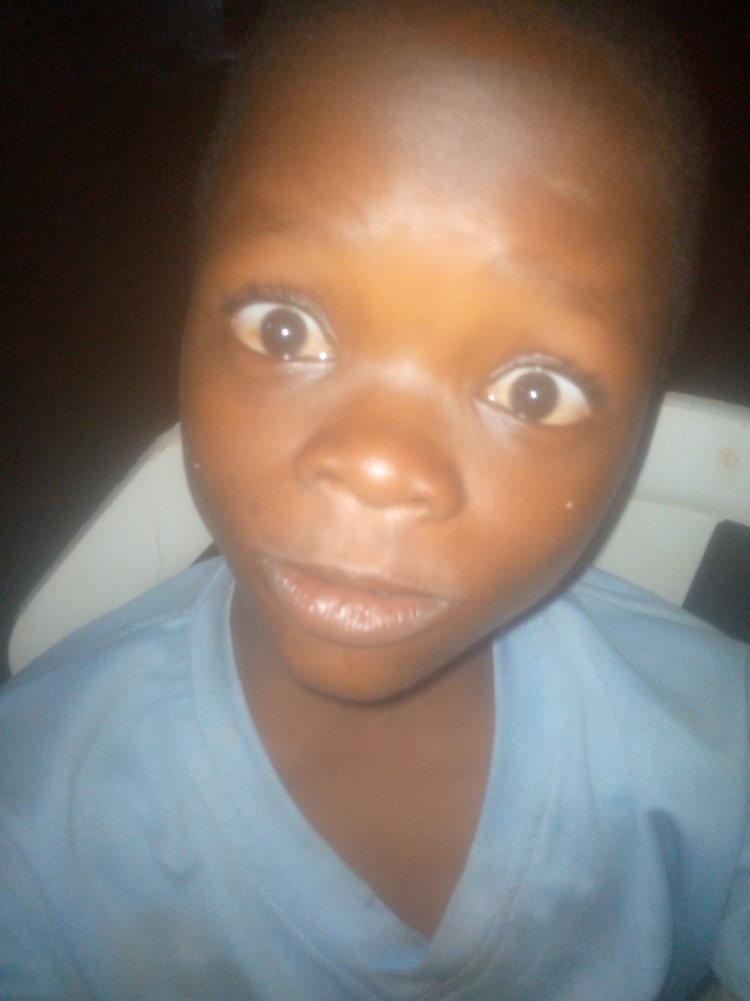 A close-up shot of a young person with dark skin and brown eyes wearing a blue collared shirt. The location and city are unknown.