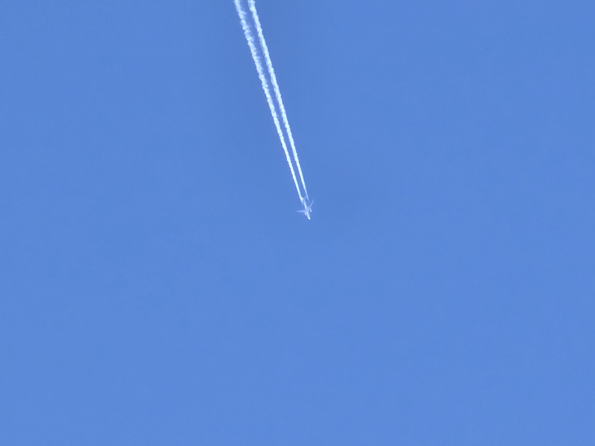 A contrail is visible in the sky above Noviy, Russia. The aircraft is leaving a trail of condensation as it moves across the sky. The contrail is bright white against the blue sky.