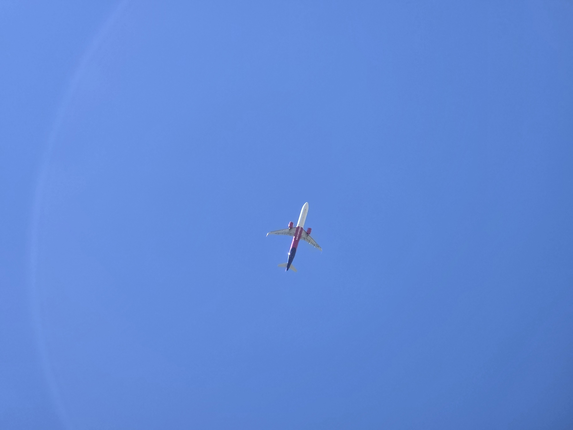 The image shows an airplane flying in a clear blue sky. The airplane is positioned in the center of the frame. The sky is uniformly blue without any clouds.
The image does not contain information about the location in the city of Varna, Bulgaria. It is not possible to determine the location from the image.
