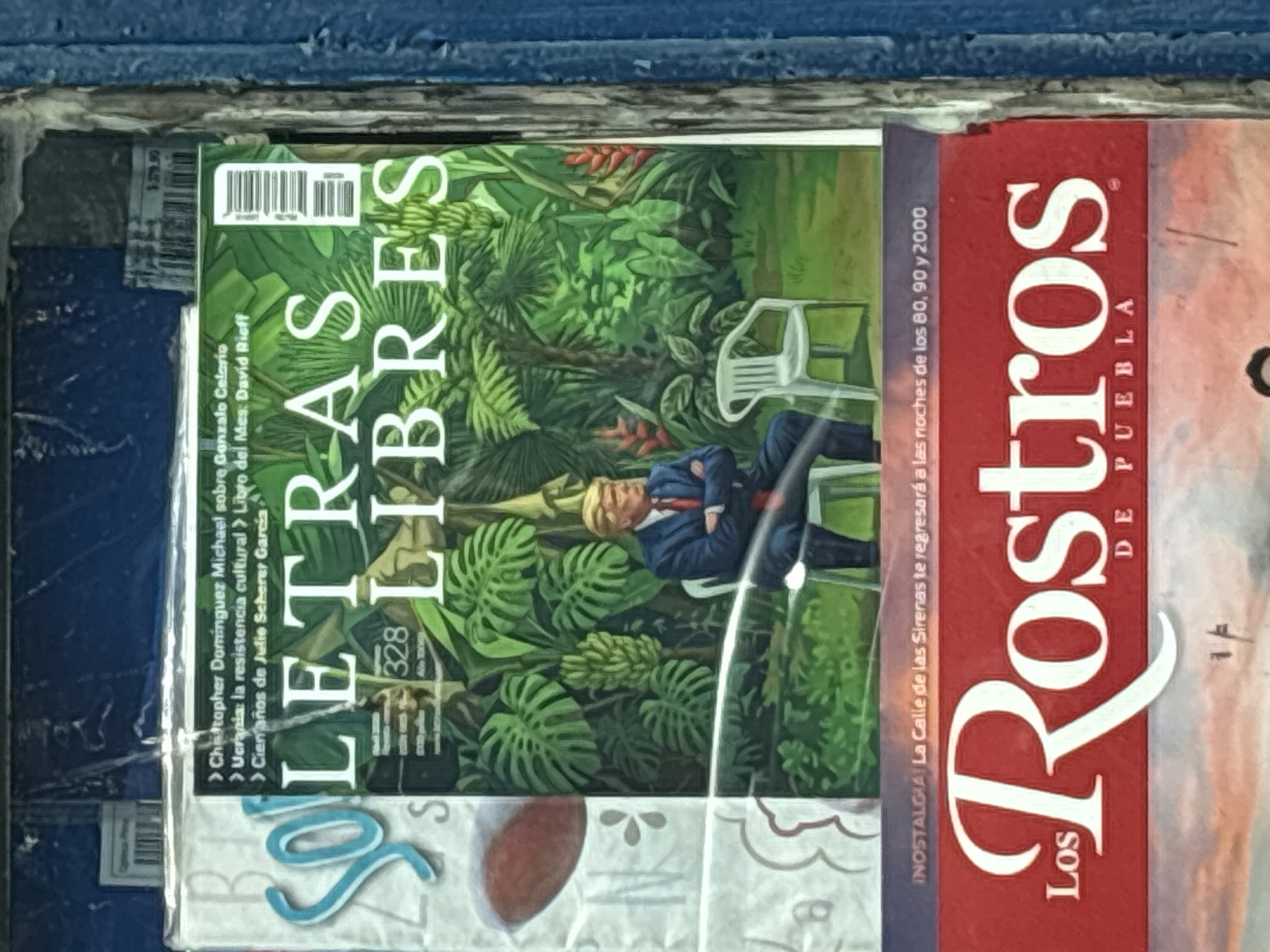 The image shows two magazines lying together, presumably in a store or newsstand. The magazine on top is "Letras Libres" with a cover featuring a green, jungle-like background with a man in a suit sitting on a white chair. The magazine beside it is "Los Rostros de Puebla". The text "DE PUEBLA" indicates the location is Puebla, Mexico. The text "INOSTALGIA! La Calle de las Sirenas te regresará a las noches de los 80, 90 y 2000" suggests the magazine covers local interest for the city of Puebla, specifically nostalgia for the 1980s, 1990s and 2000s.