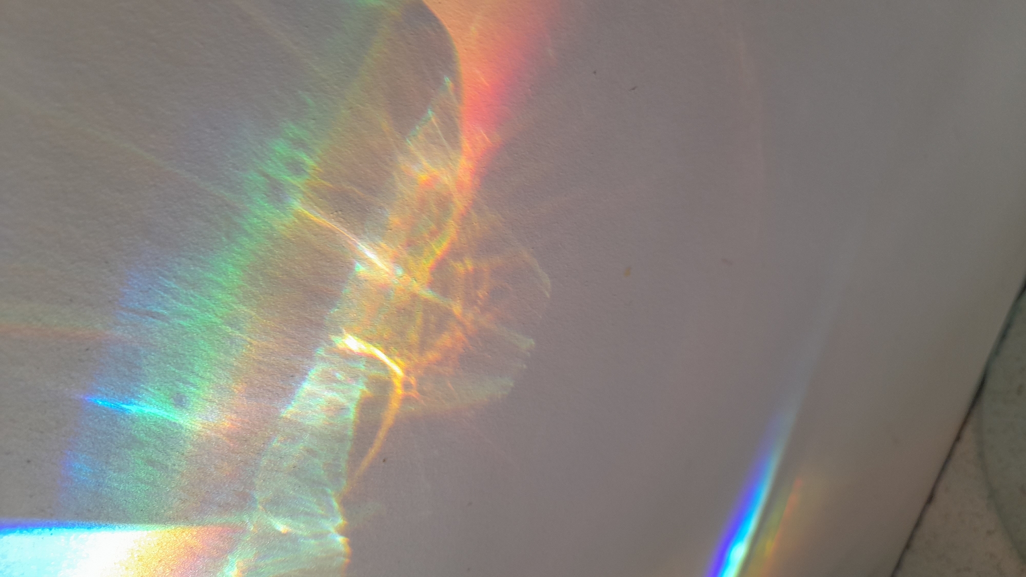 The image shows a rainbow pattern on a white wall. The rainbow is likely caused by sunlight refracting through a prism or other refractive object. The location is unknown but presumed to be in Saint Petersburg, Russia. The scene is indoors. There are no people, subjects, objects, actions, or interactions visible other than the rainbow on the wall.