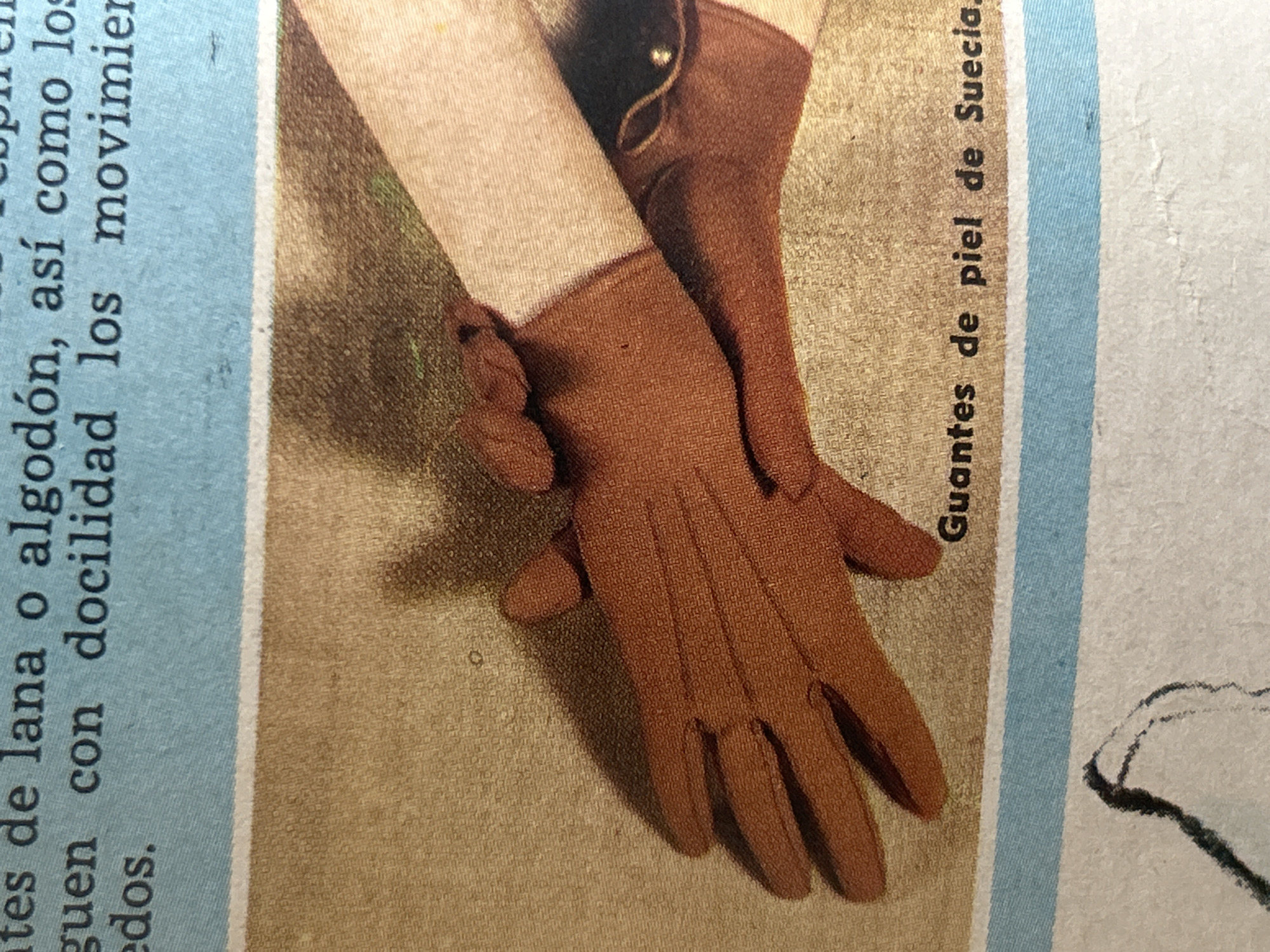 The image shows a close-up of a pair of brown leather gloves, possibly made of Swedish leather, as indicated by the Spanish text "Guantes de piel de Suecia" at the bottom. The gloves are positioned on a textured surface that appears to be a fabric background, possibly a tan or light brown tablecloth or garment. The gloves are shown from a side view, with the fingers extended. One glove is slightly in front of the other. There is also a portion of a light-colored sleeve visible on the right side, suggesting the gloves are being worn. The background above the gloves features lines of text in Spanish printed on a light blue surface, which is likely part of a magazine or book page. The text is partially visible and appears to be describing materials like wool or cotton. The lower portion of the image shows a white background with some faint, dark lines that may be part of a drawing or another illustration. There is no identifiable information or context within the image that links it to Santa Ana, Venezuela, or any specific city.